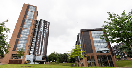 Tall brick buildings with glass windows on a grassy hill under a cloudy sky.