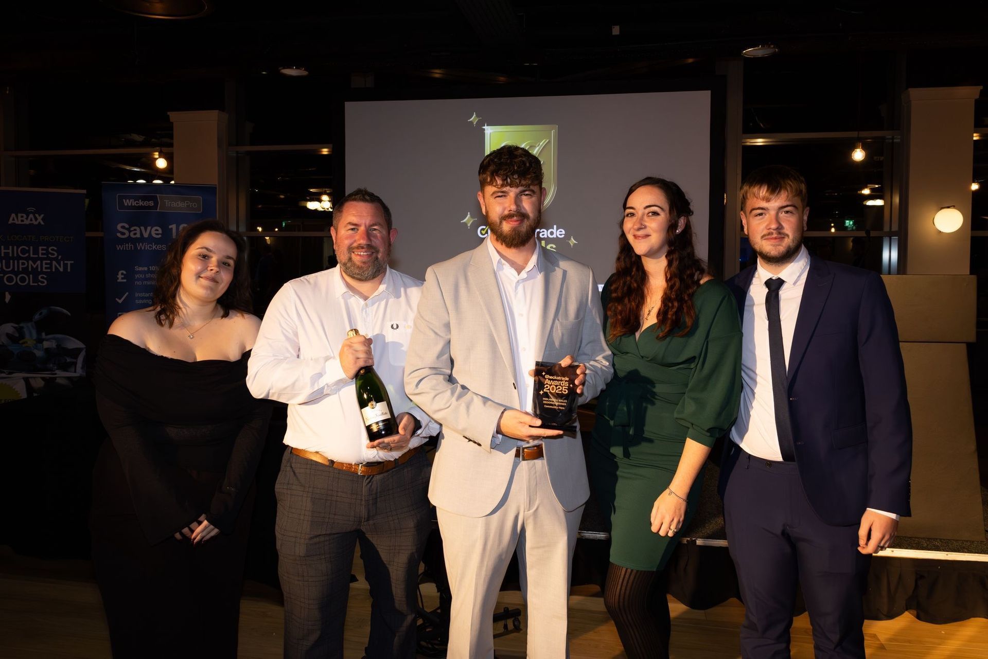 People holding an award and a bottle of champagne at an event, some wearing formal attire.