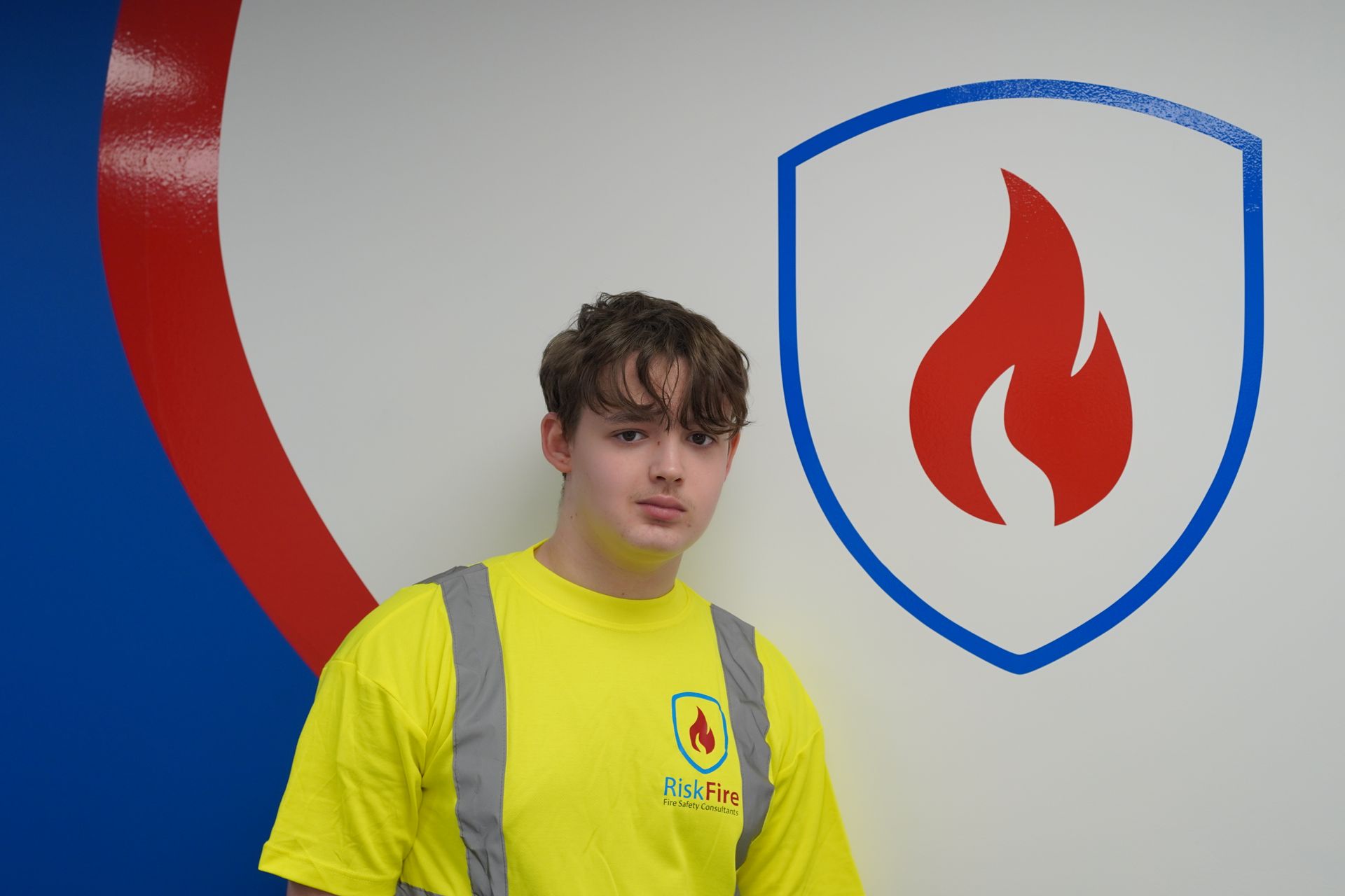 Man in yellow safety vest stands next to a wall with a flame logo.