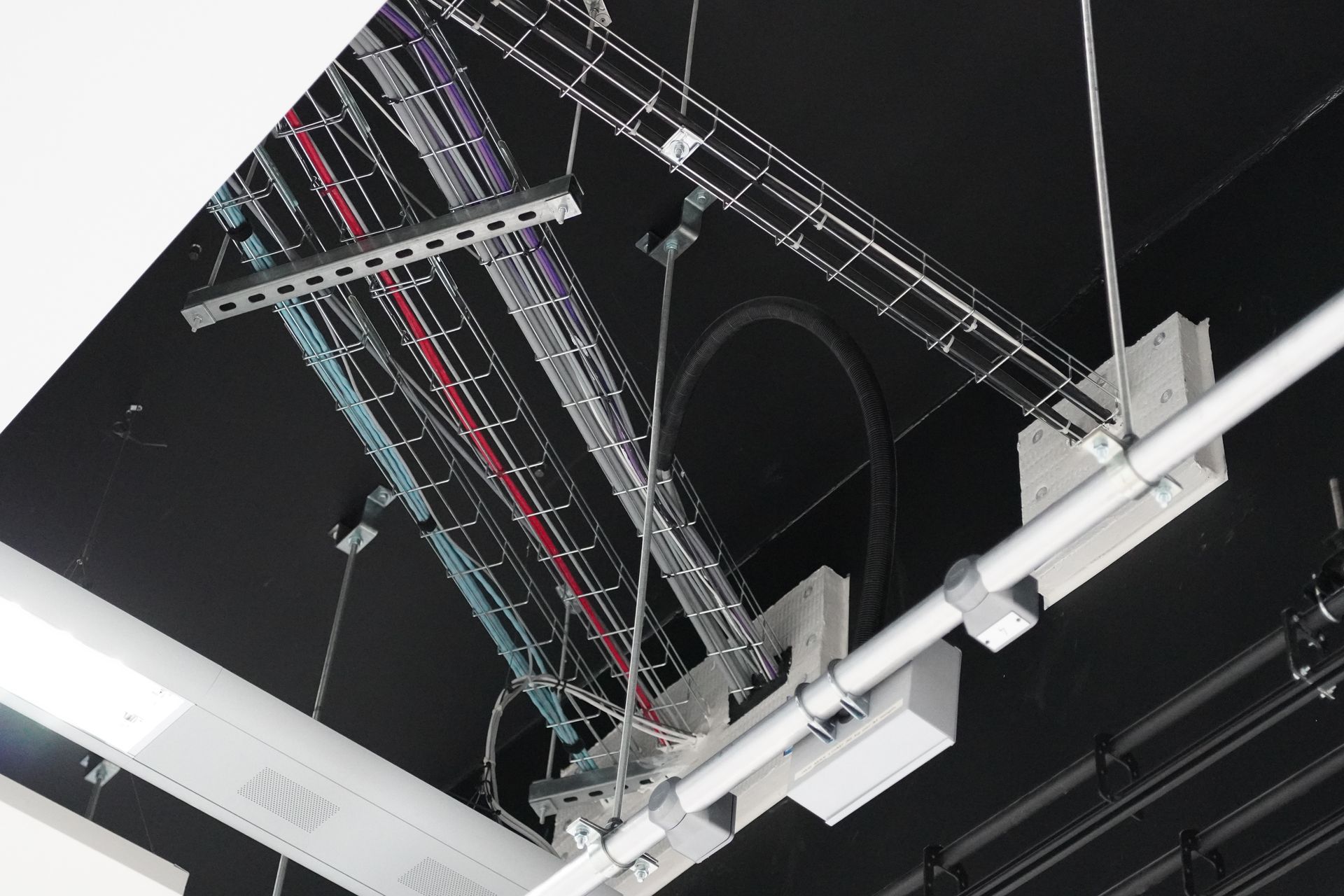 Overhead view of a black ceiling with many organized cables secured to metal structures.