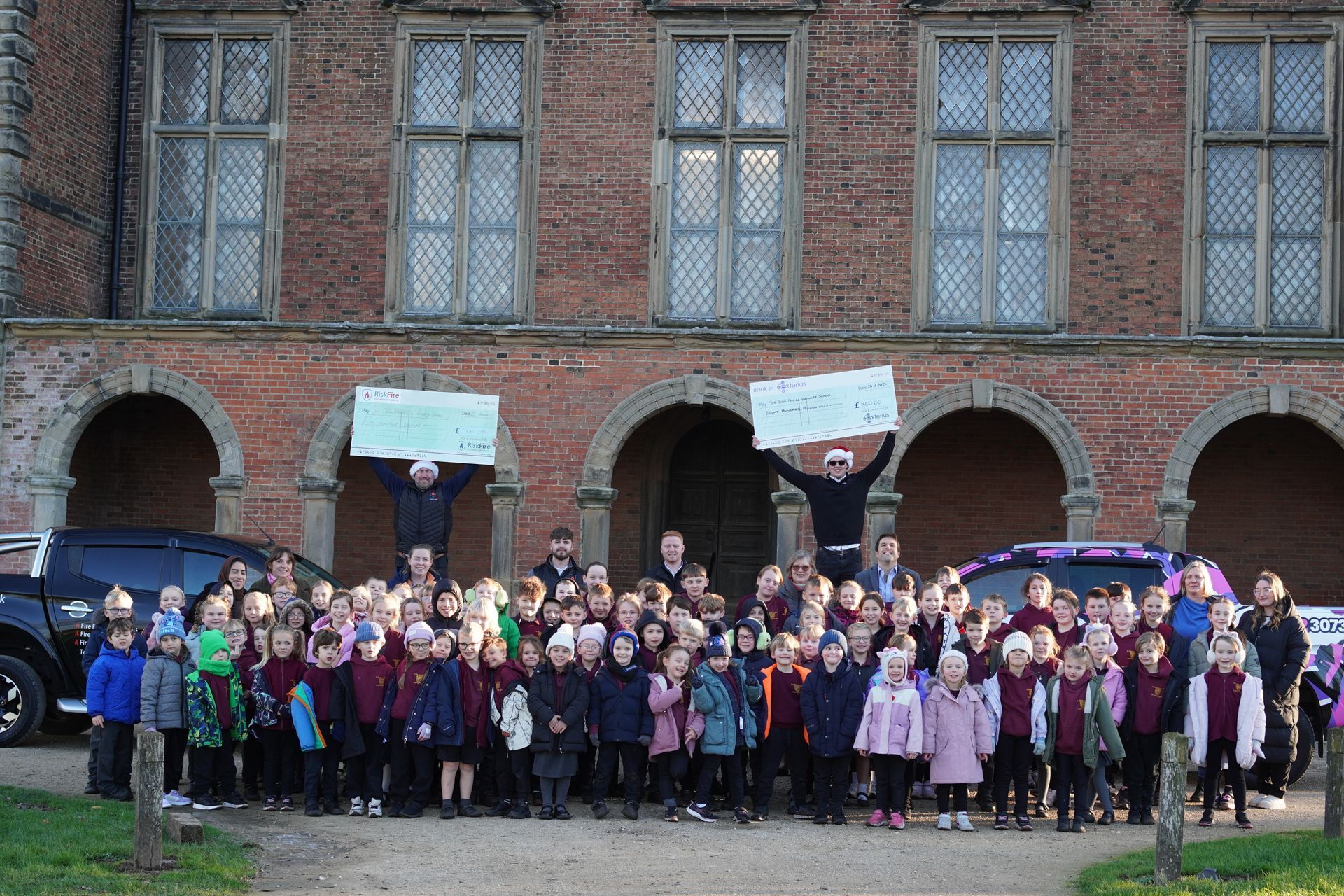 Large group of children in front of a brick building, holding signs. Two adults hold signs above the group.