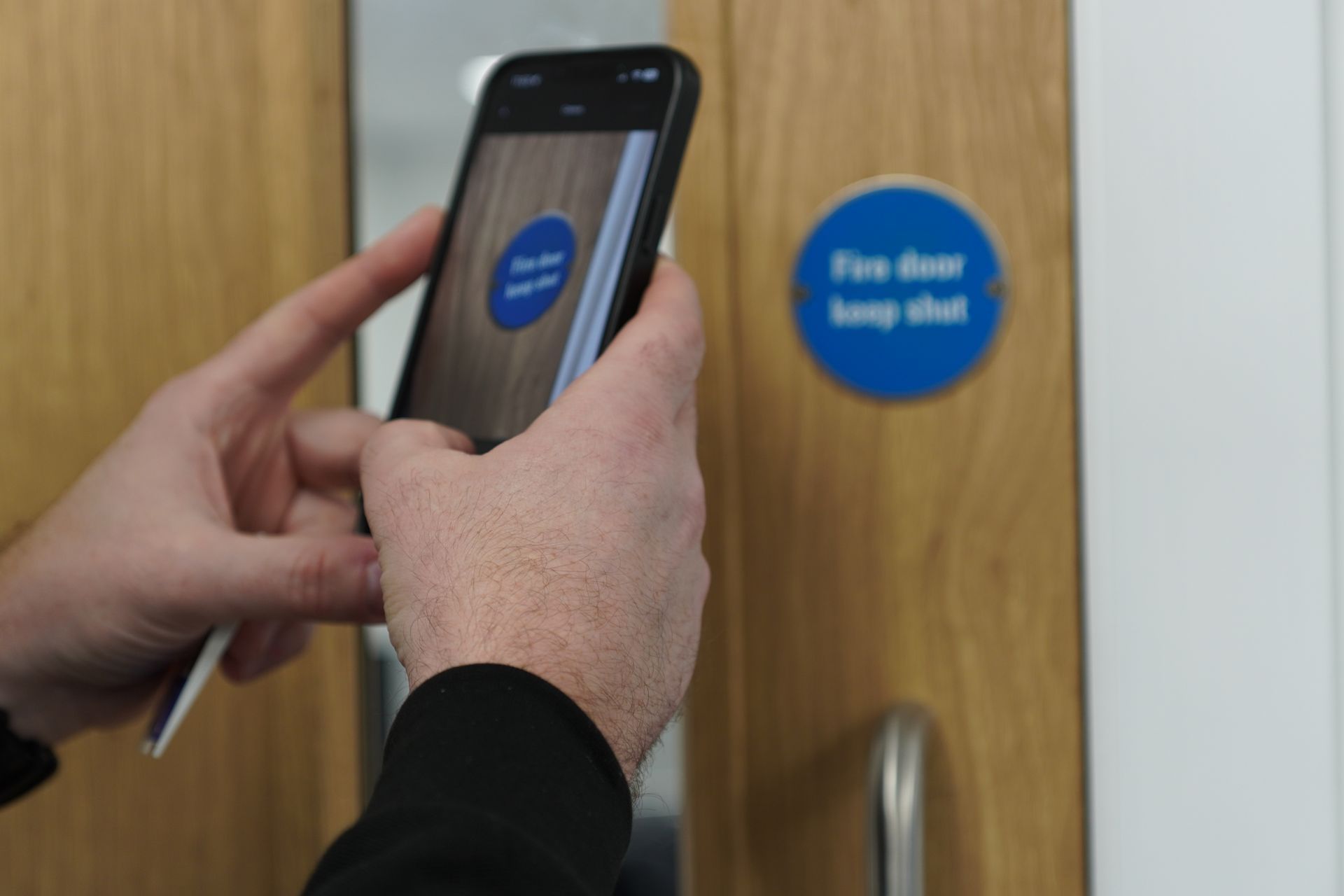 Person holding phone, scanning fire door label. Blue and white sign reads 