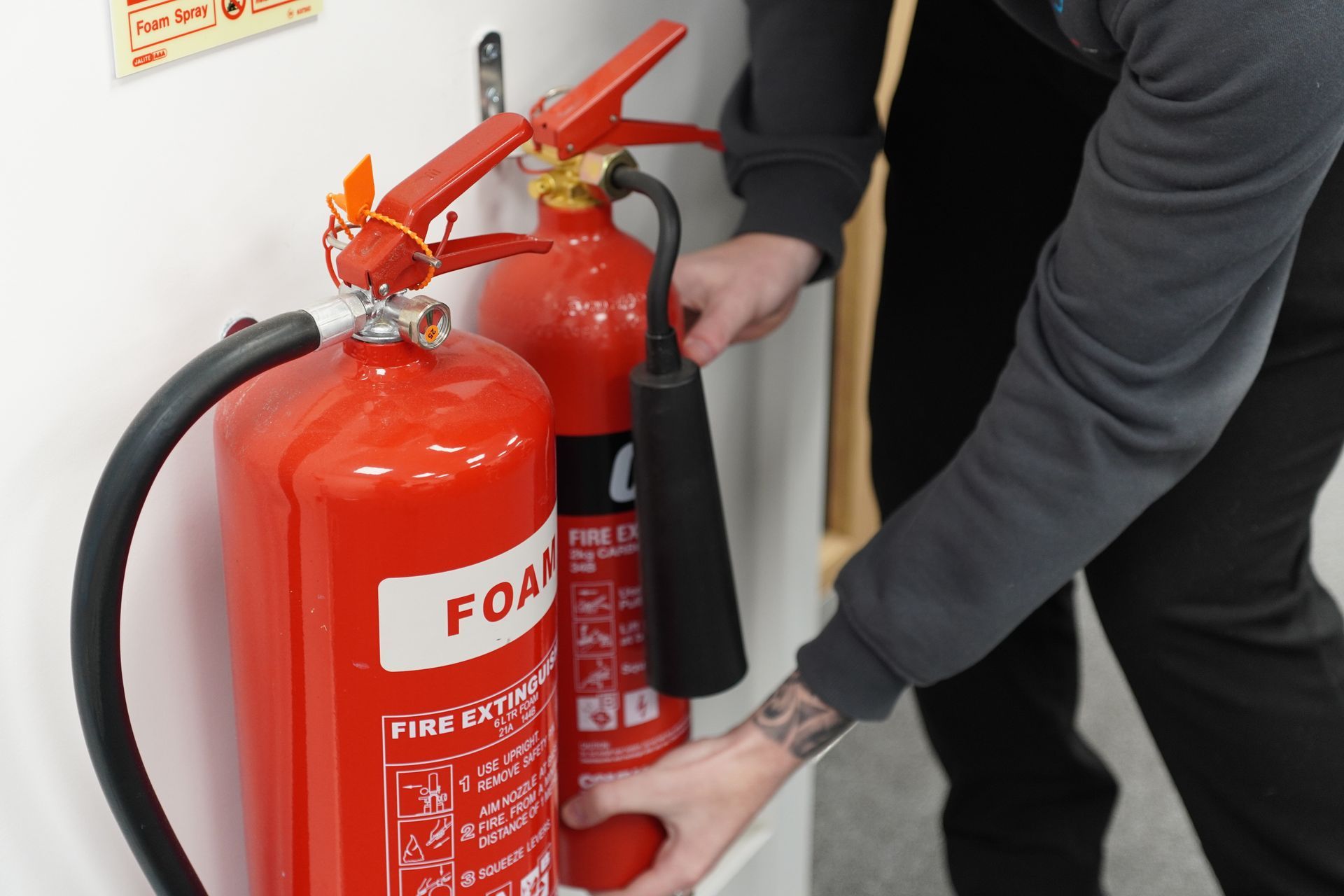 Person taking down a red fire extinguisher from a wall.