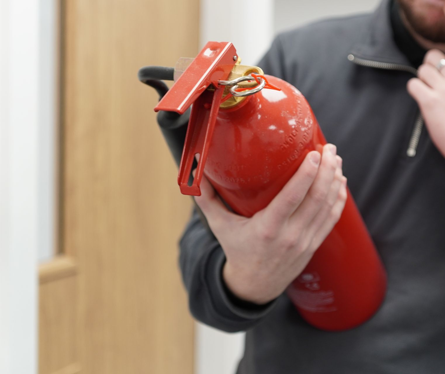 Person holding a red fire extinguisher, indoors, preparing for use.