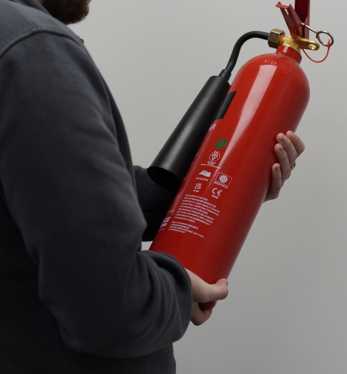 Person holding a red fire extinguisher, black hose, against a neutral background.