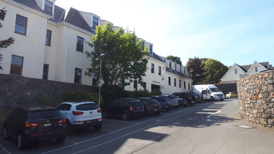 Cars parked in front of a light-colored building with multiple windows; sunny day.