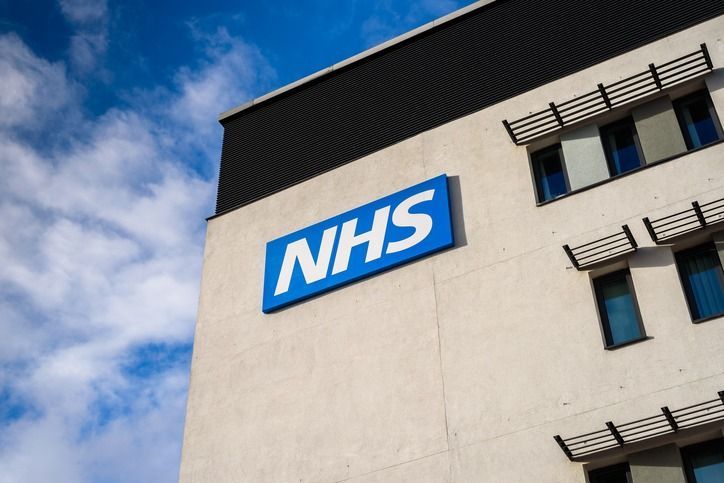 NHS building with blue and white logo against a cloudy sky.