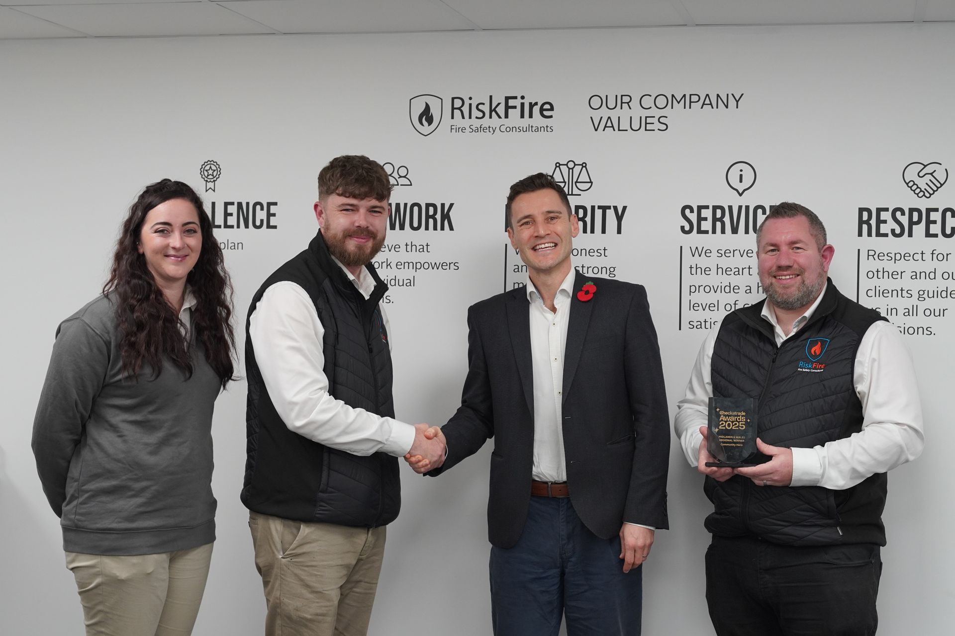 Four people shaking hands in front of a company values wall. Two hold awards.