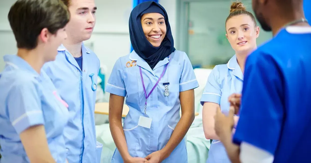 Medical team in blue scrubs, smiling, gathered in a hospital room, conversing.