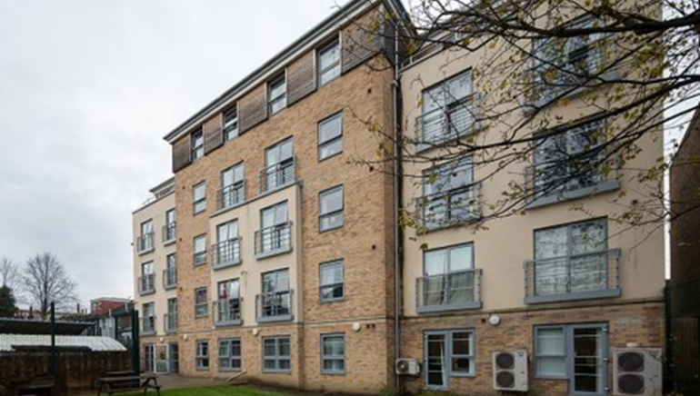 Multi-story apartment building with brick and beige facades, balconies, and green lawn.