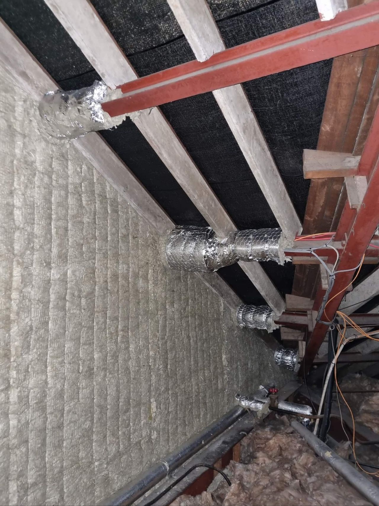 Interior view of an attic space with ductwork and insulation, showing metal beams and reflective surfaces.