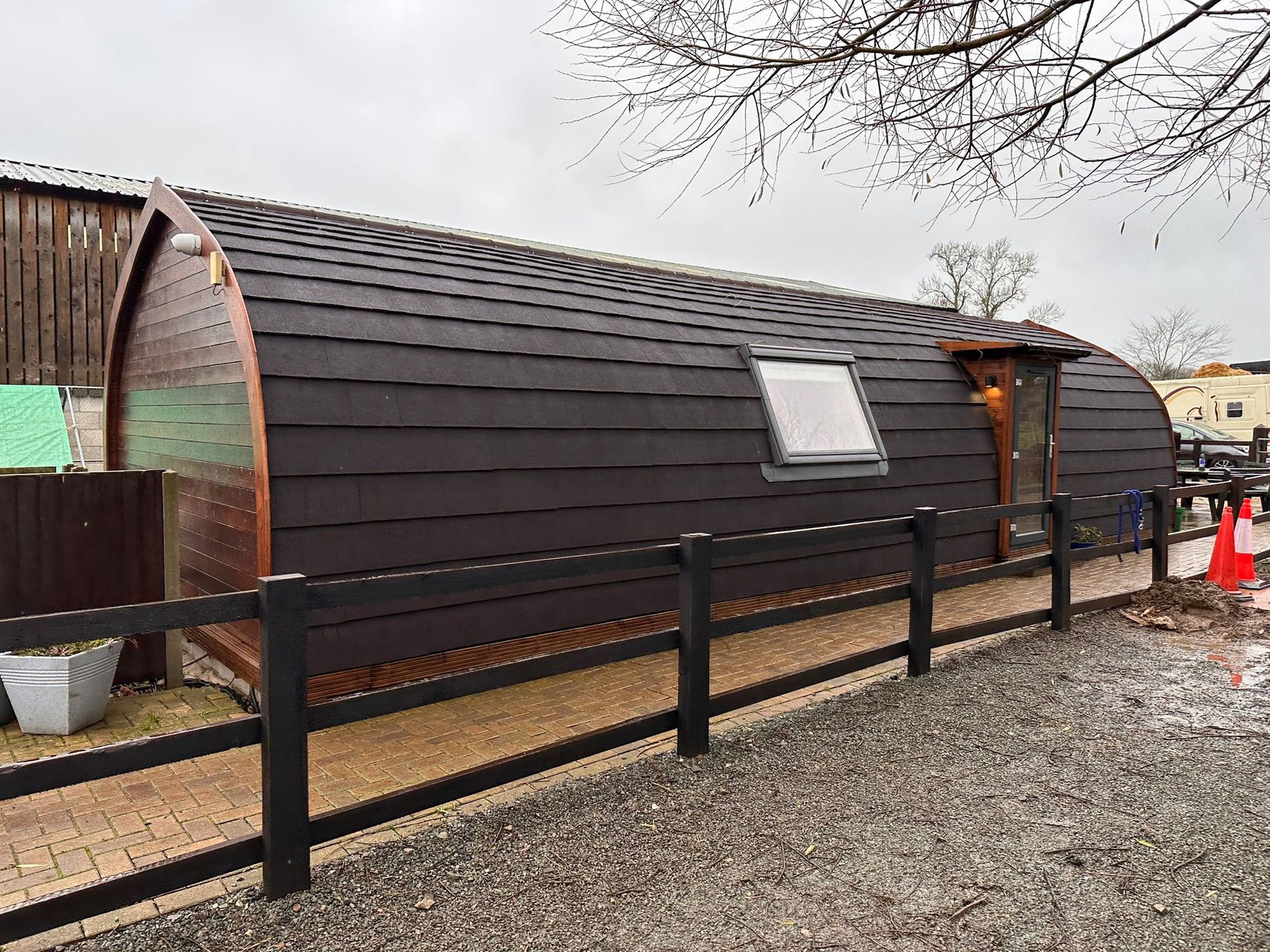 Dark brown glamping pod with small window and wooden fence.