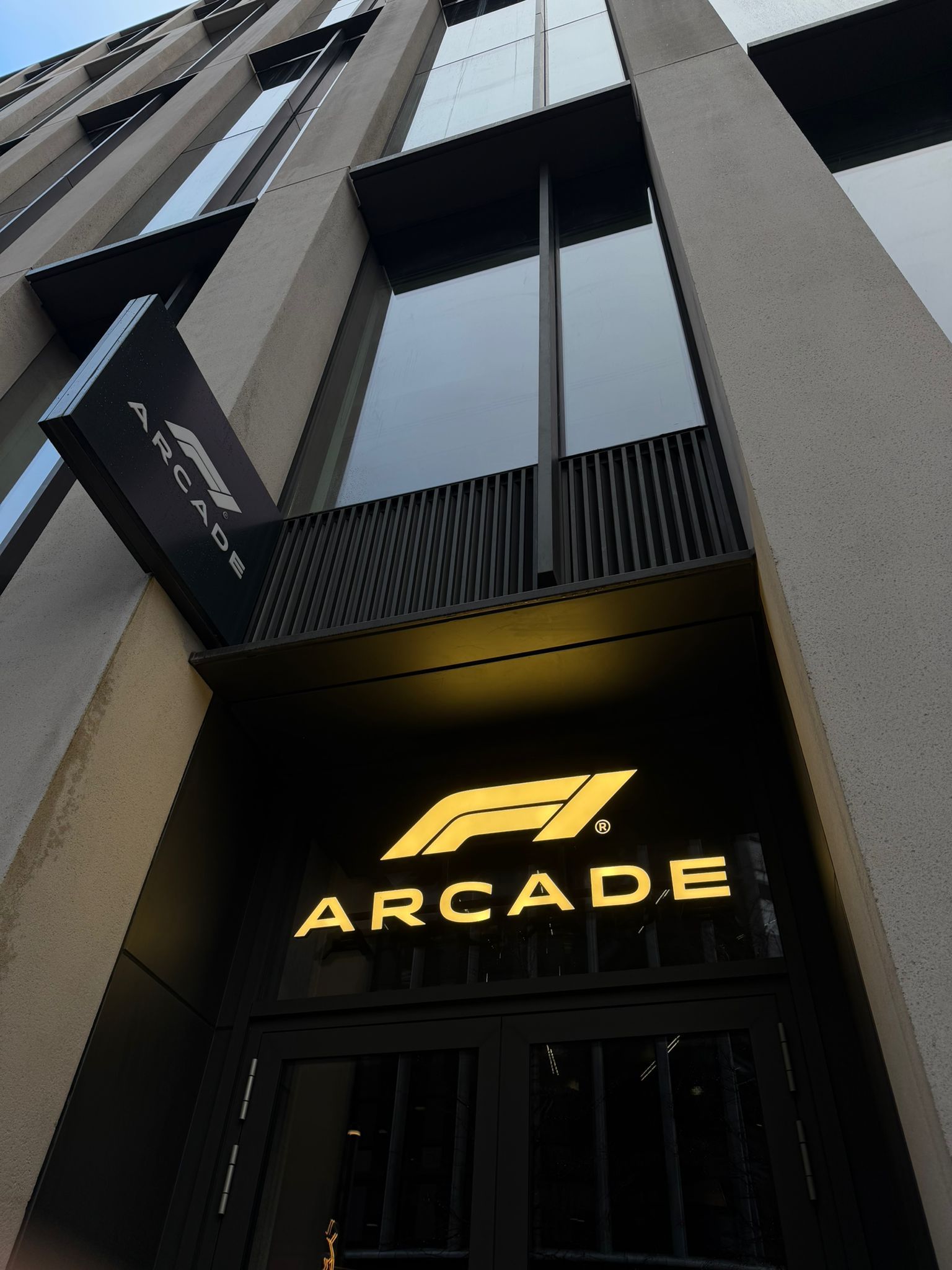 Entrance to the F1 Arcade in a modern building; a sign with the logo is above the doors.
