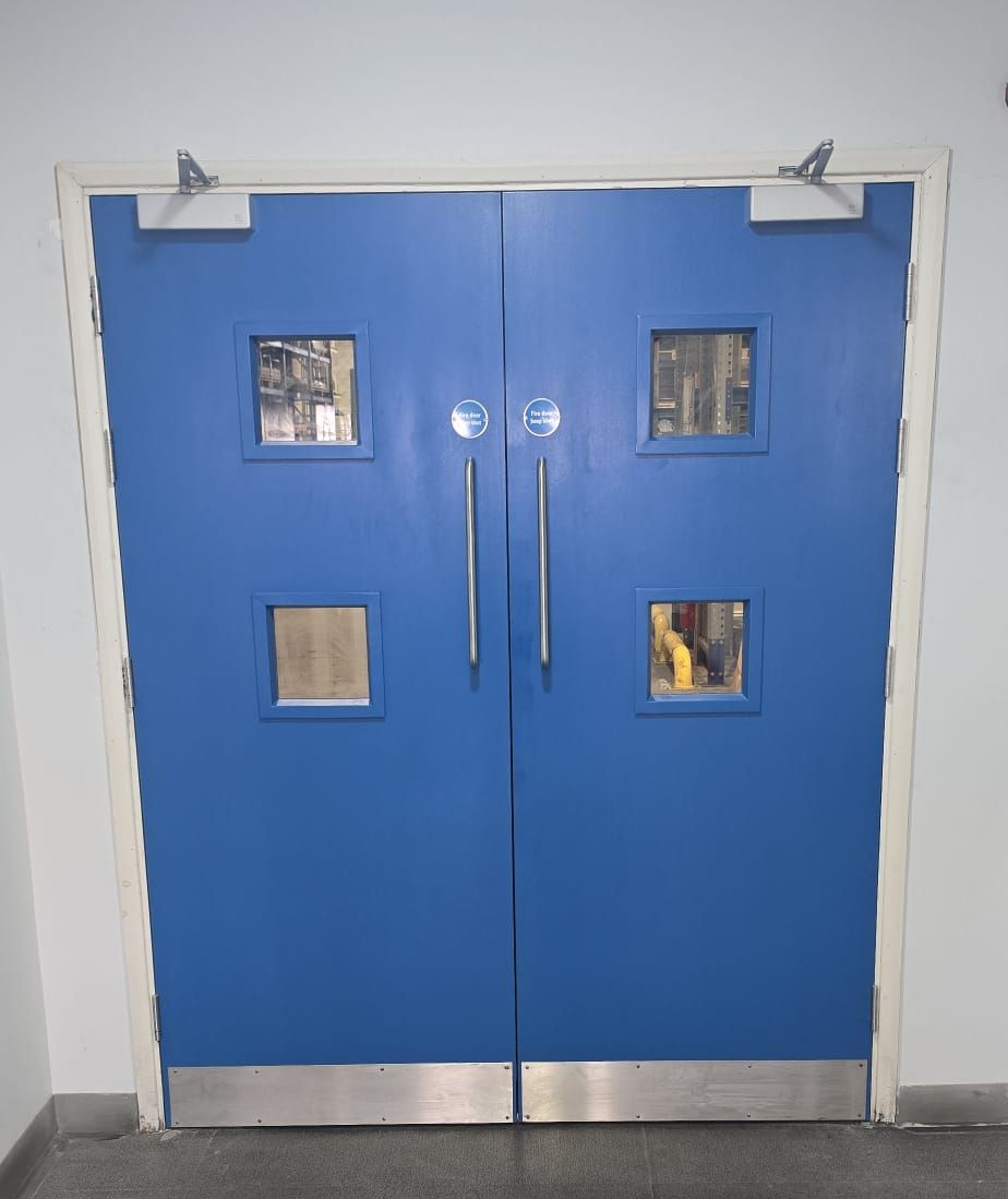 Blue double doors with small square windows, silver handles, and a metal kick plate.