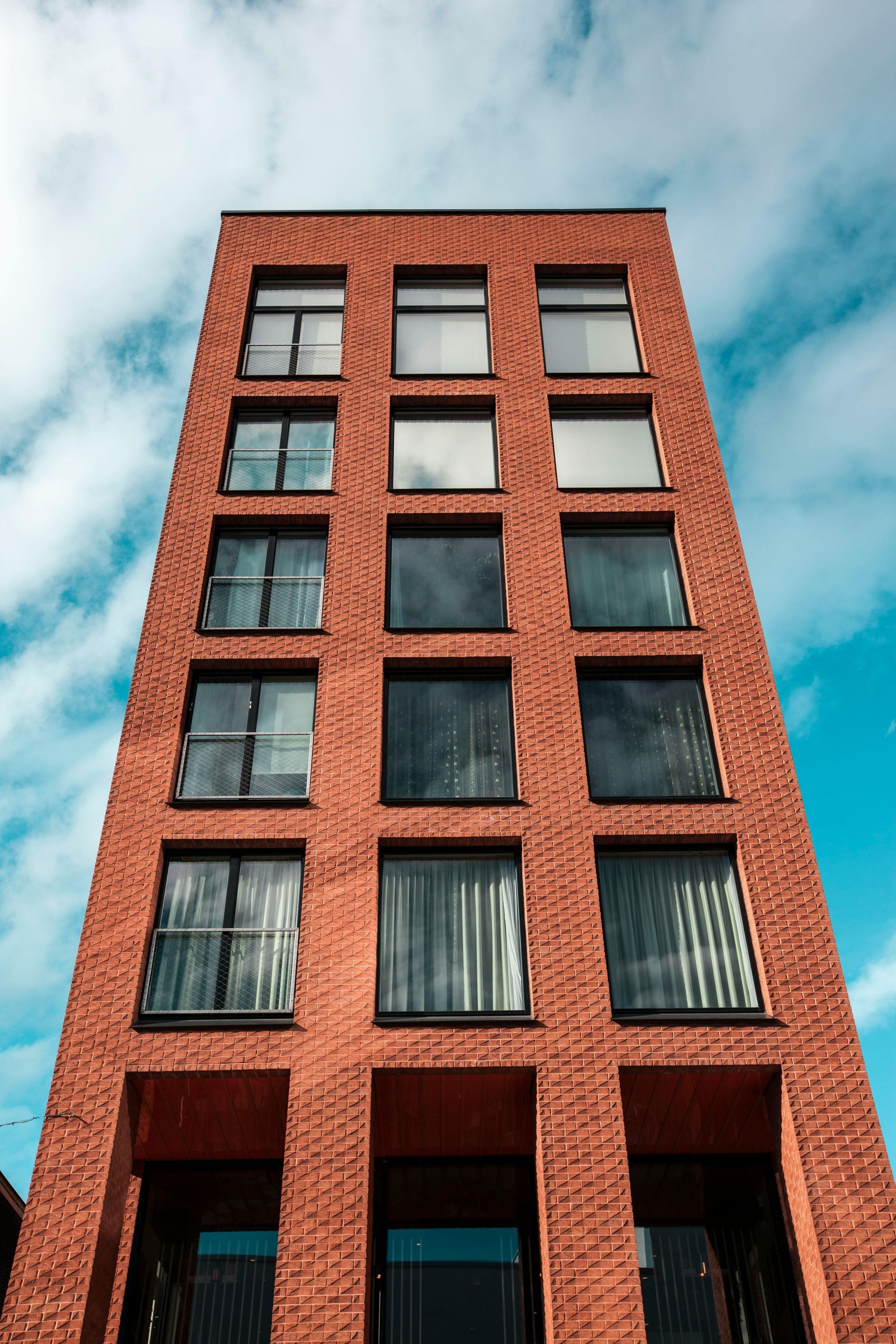 Red brick building with rows of windows against a blue sky with clouds.