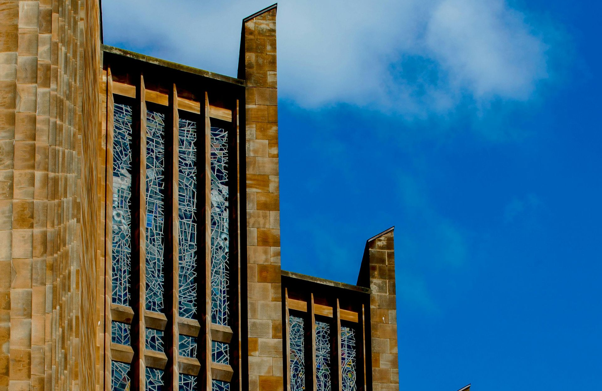Tall, stone church facade with vertical stained glass windows against a bright blue sky.