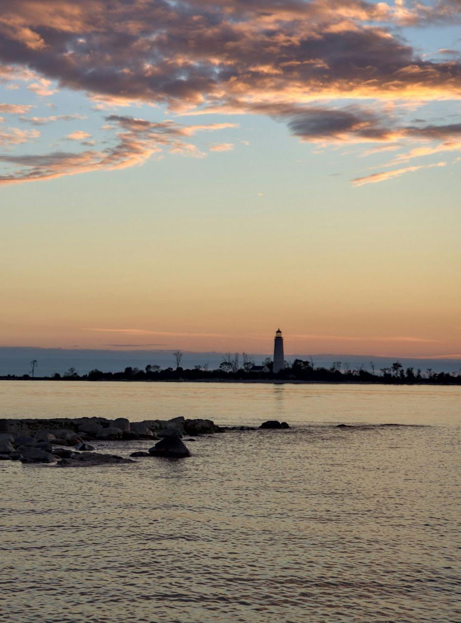 Lighthouse silhouetted against a colorful sunset sky over calm water.
