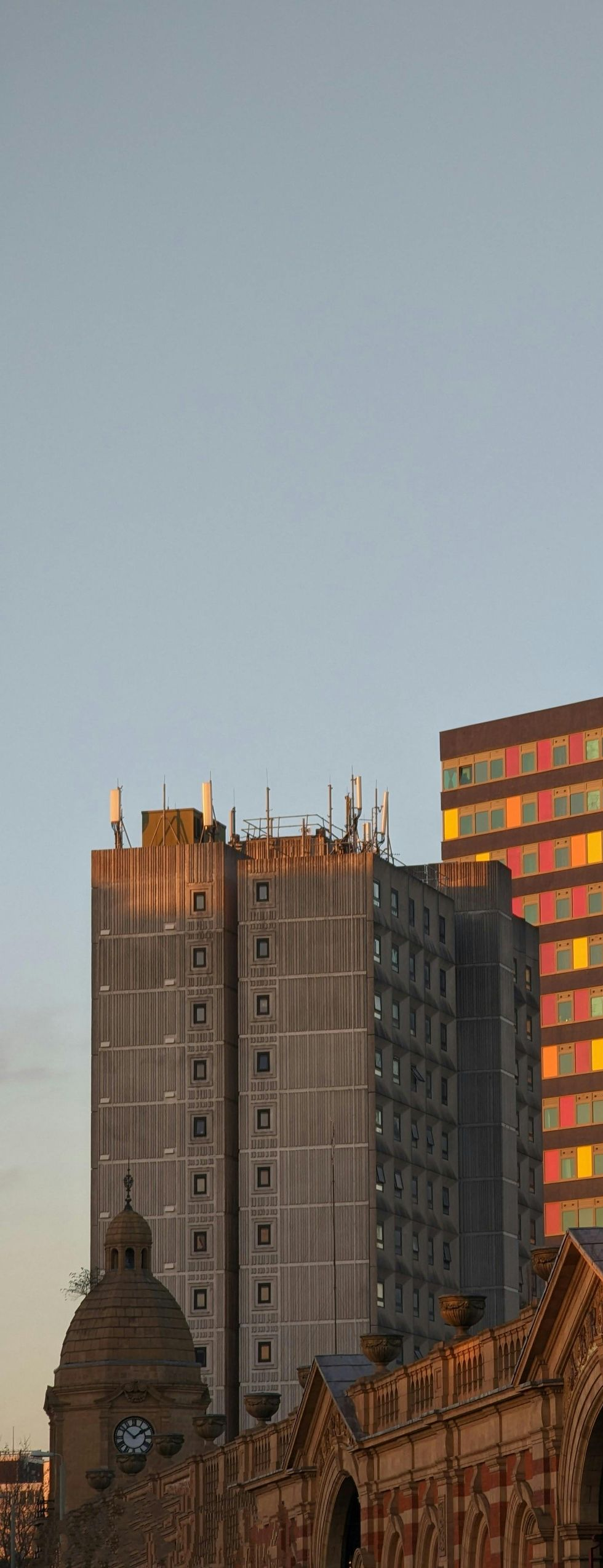 City skyline with tall buildings, some illuminated in golden sunlight, against a clear sky.