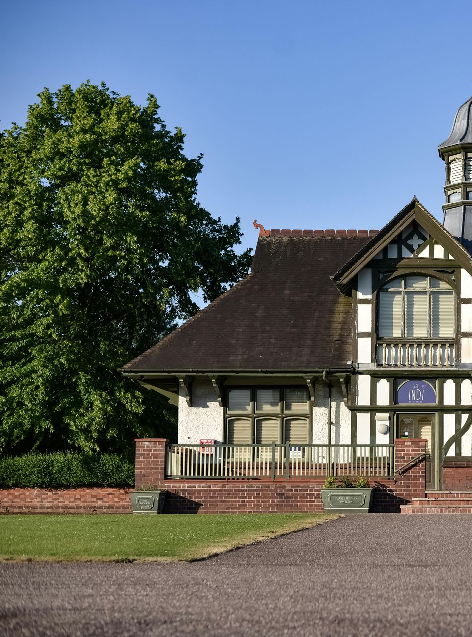 Two-story Tudor style house with green trim, brown roof, and a large tree in the background.