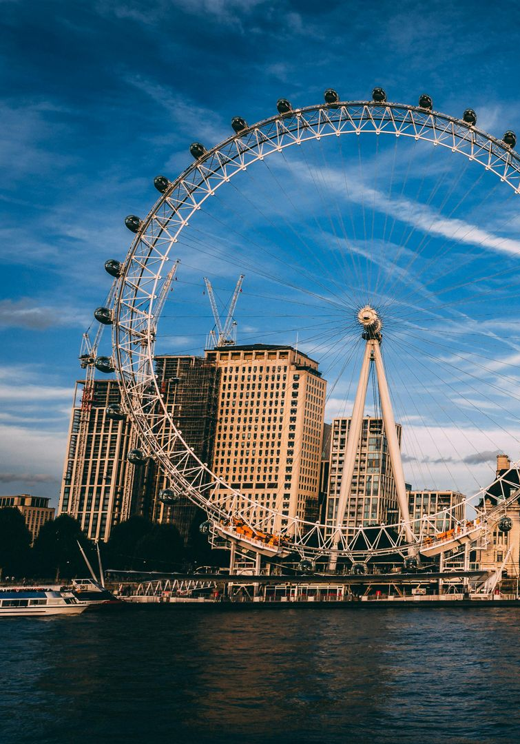 London Eye Ferris wheel against blue sky, with buildings and river in foreground.