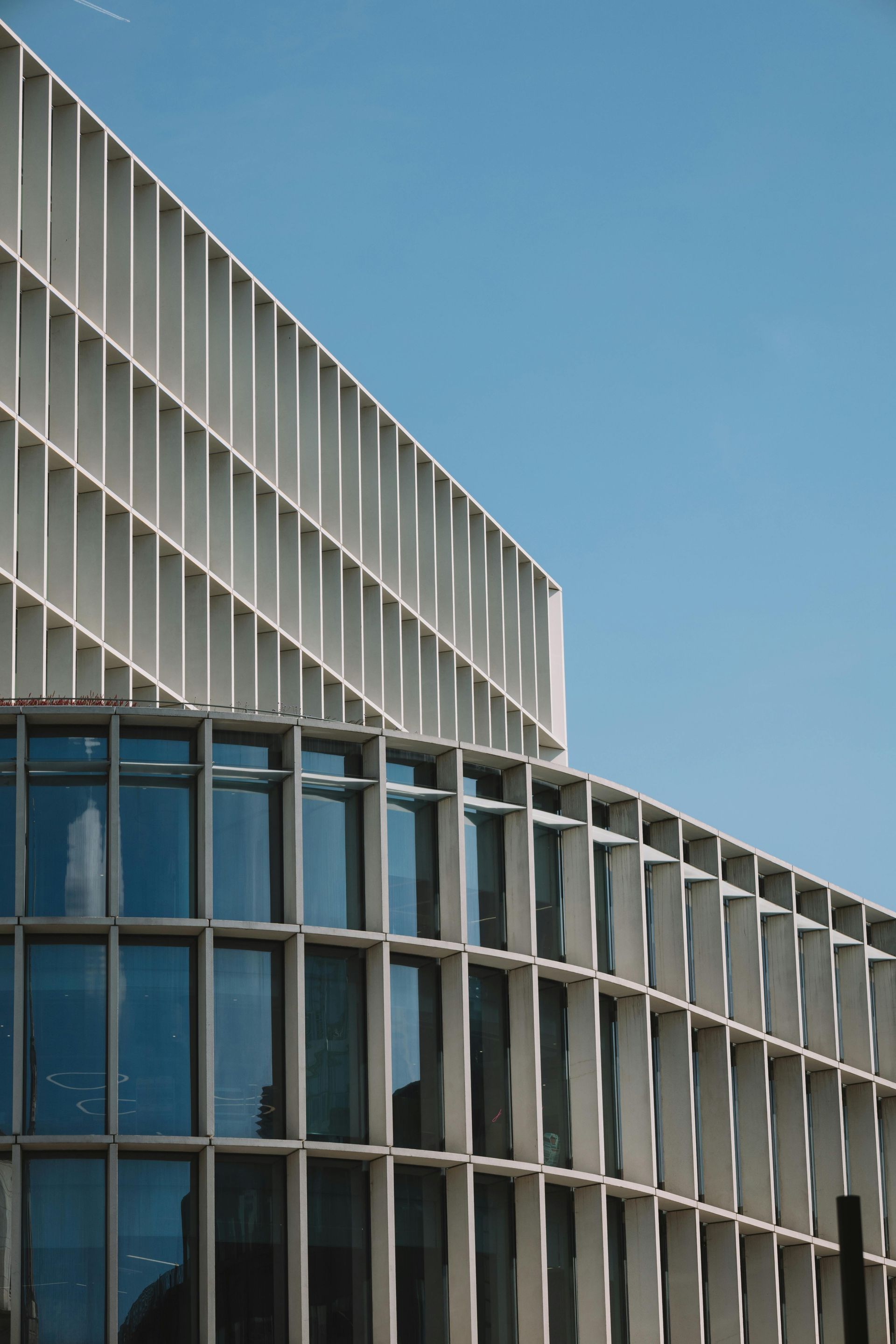 Modern building facade with white vertical fins and blue-tinted windows against a clear sky.