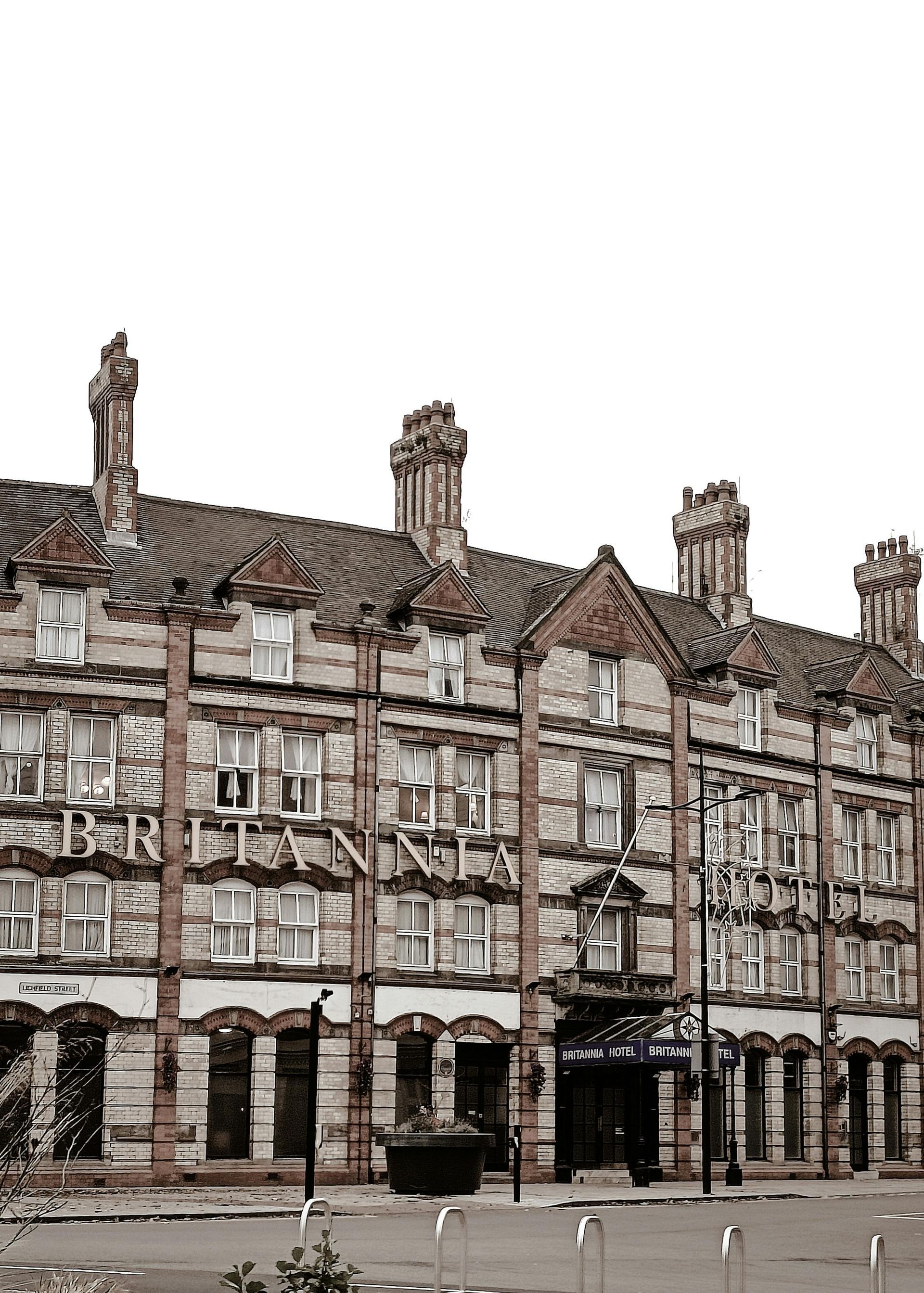 Multi-story brick building with ornate facade, chimneys, and arched doorways against a white sky.