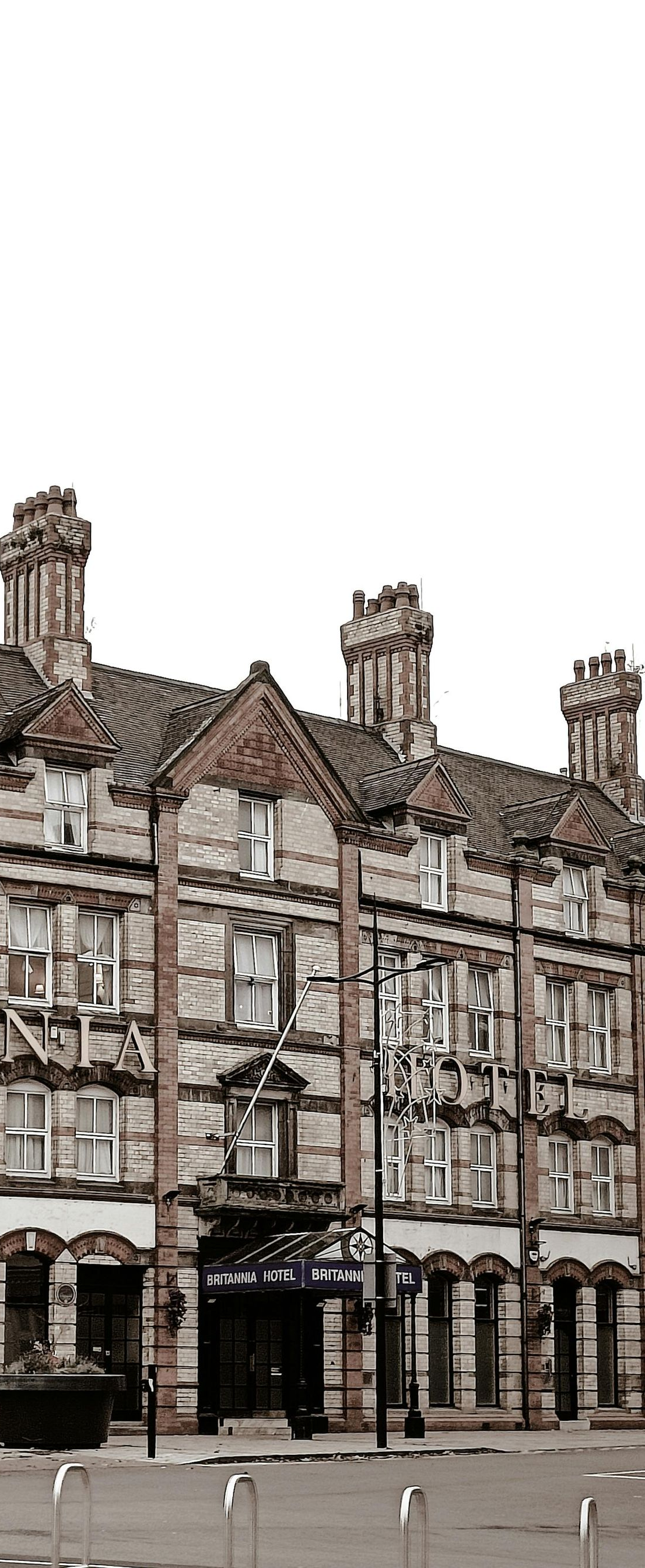 A multi-story brick building with ornate windows, topped with chimneys, along a street.