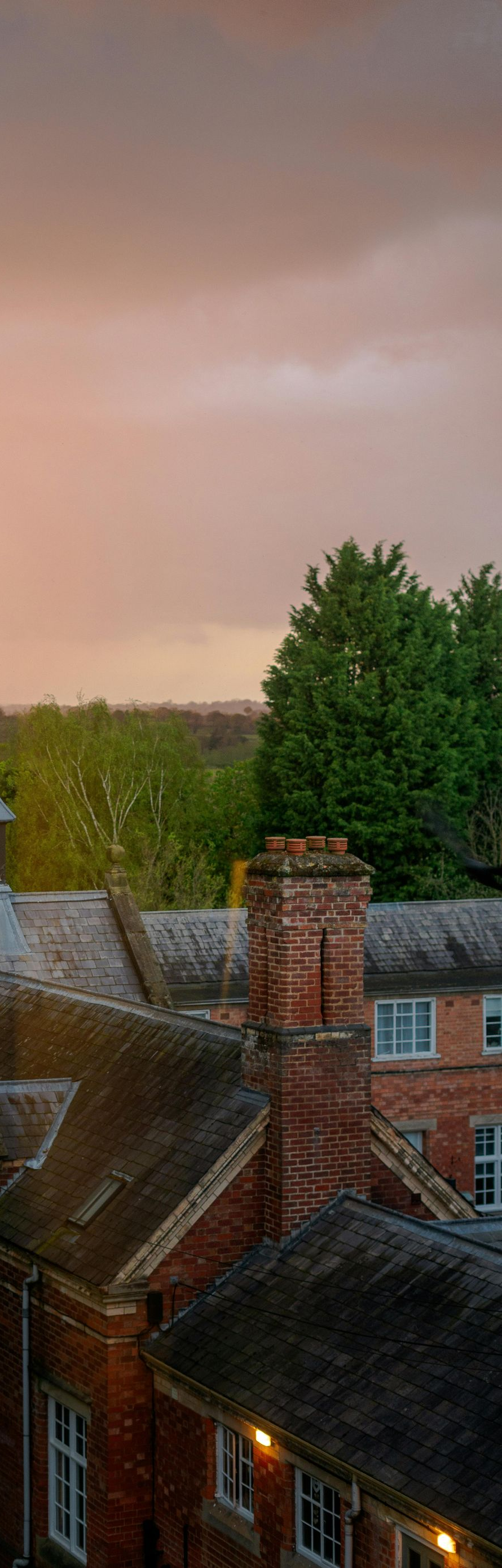 Roofs of brick buildings with a chimney, under a pink and orange cloudy sky.