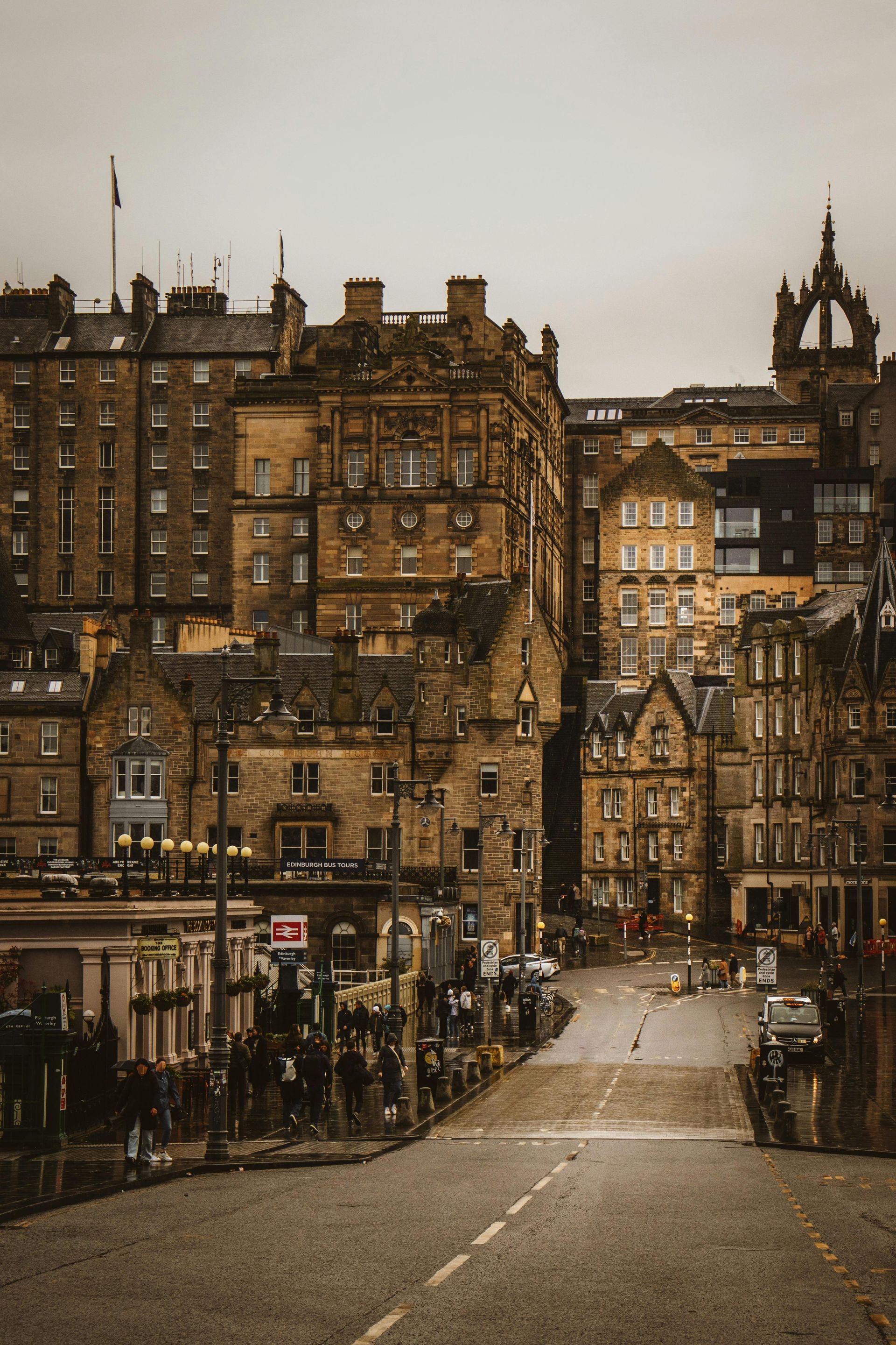 Stone buildings line a street sloping downhill in Edinburgh, Scotland. Overcast sky.