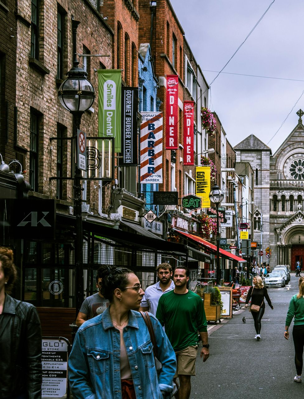 Street scene in Dublin, Ireland, lined with shops and signs, people walking, church in background.