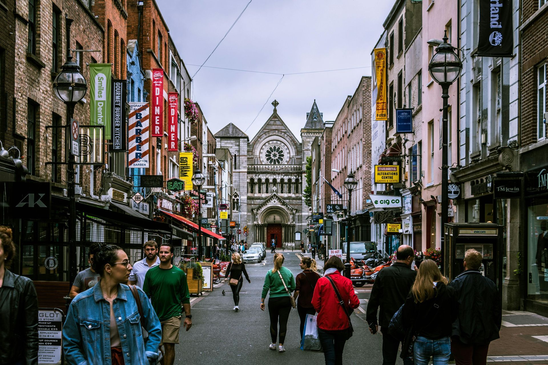 Street scene in Dublin, Ireland, with people walking towards a large church. Shops and banners line the street.