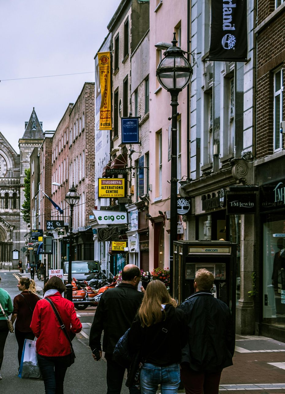 Street scene in Dublin, Ireland. Pedestrians walk past shops under cloudy skies.