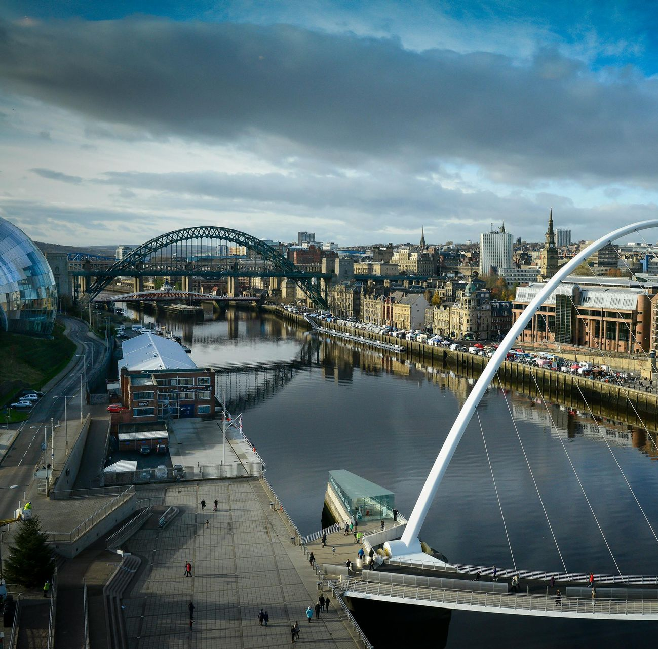 Newcastle upon Tyne cityscape with river, bridges, and modern architecture. Cloudy sky.