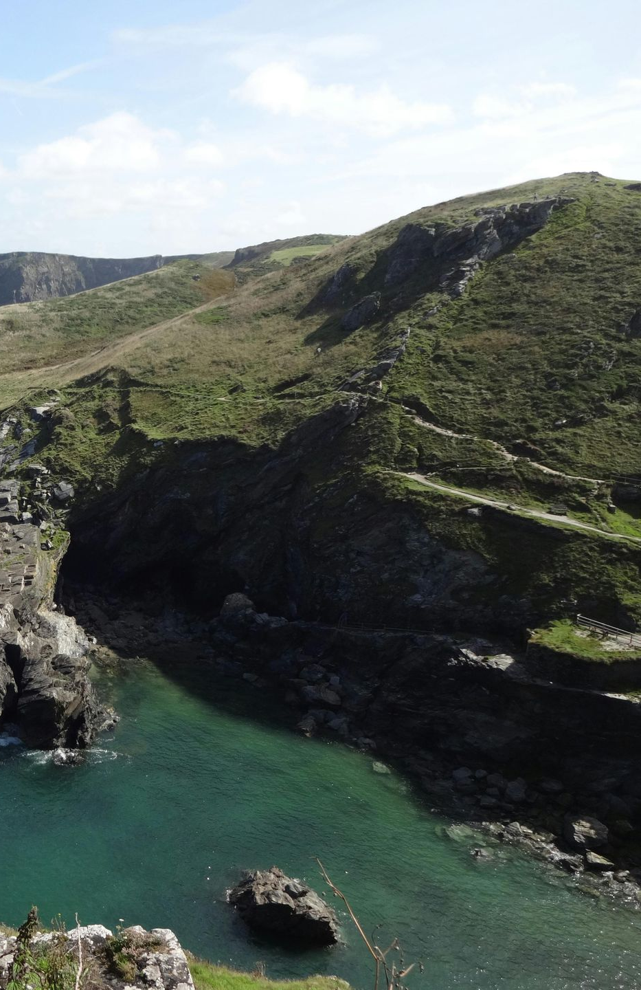 Coastal view: turquoise water, green hills, rocky cliffs, and bright sky.