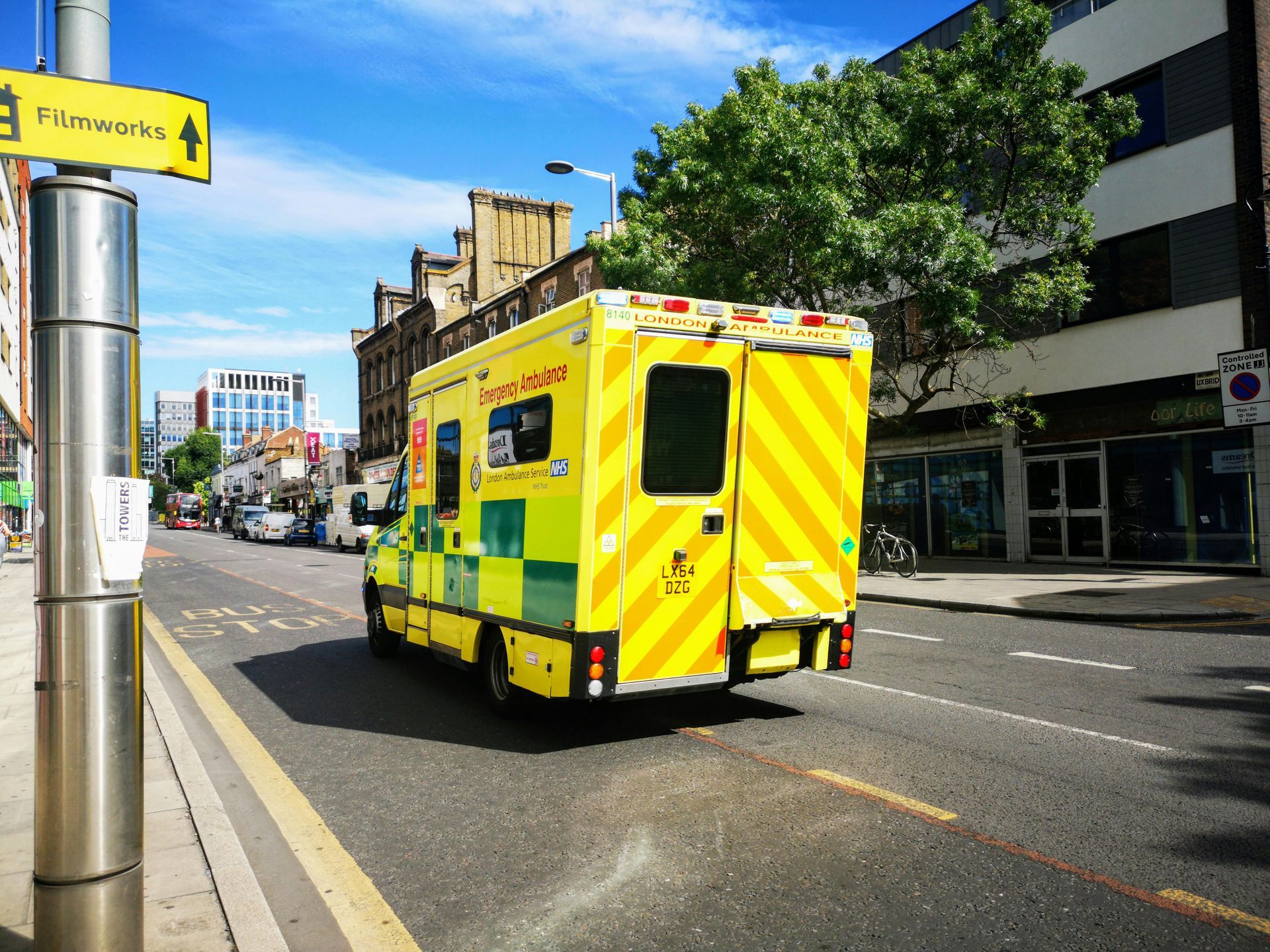 Yellow ambulance driving down a city street on a sunny day.