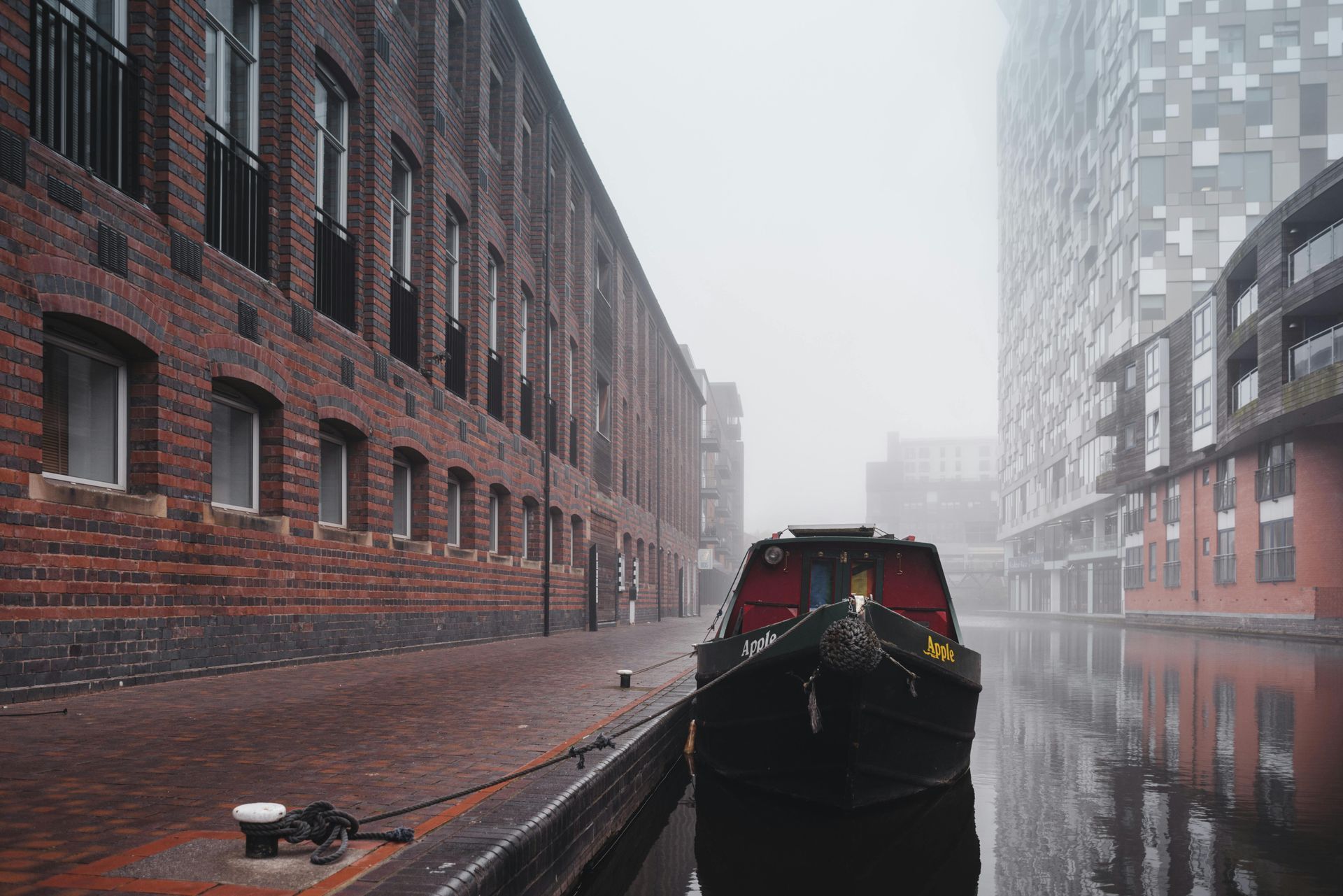 Canal boat in a brick-lined waterway, misty day. Buildings on either side.
