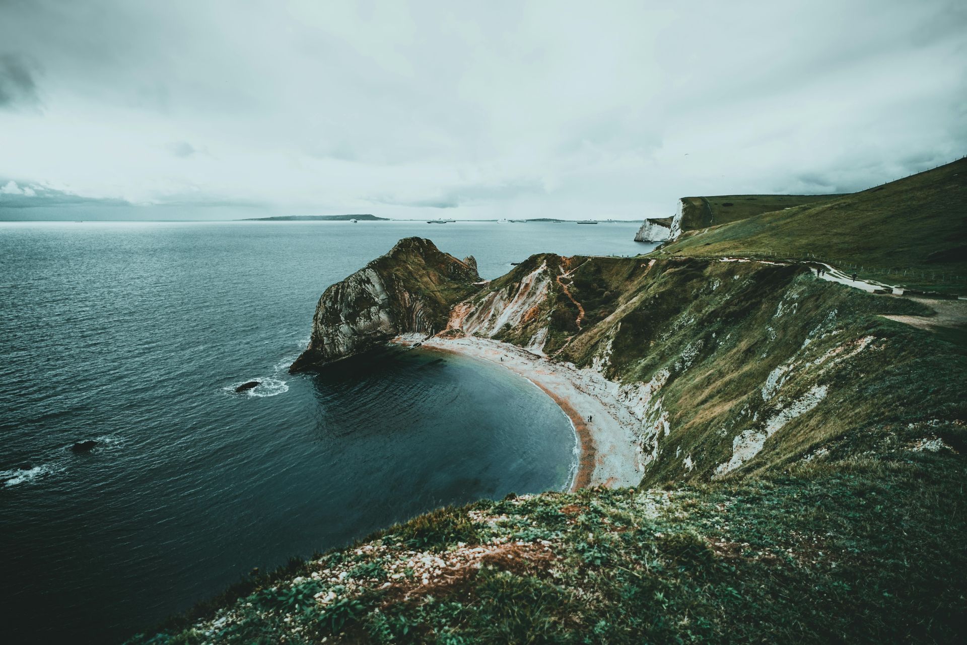 Coastal cliffs with a rocky beach below, overcast sky over the water.