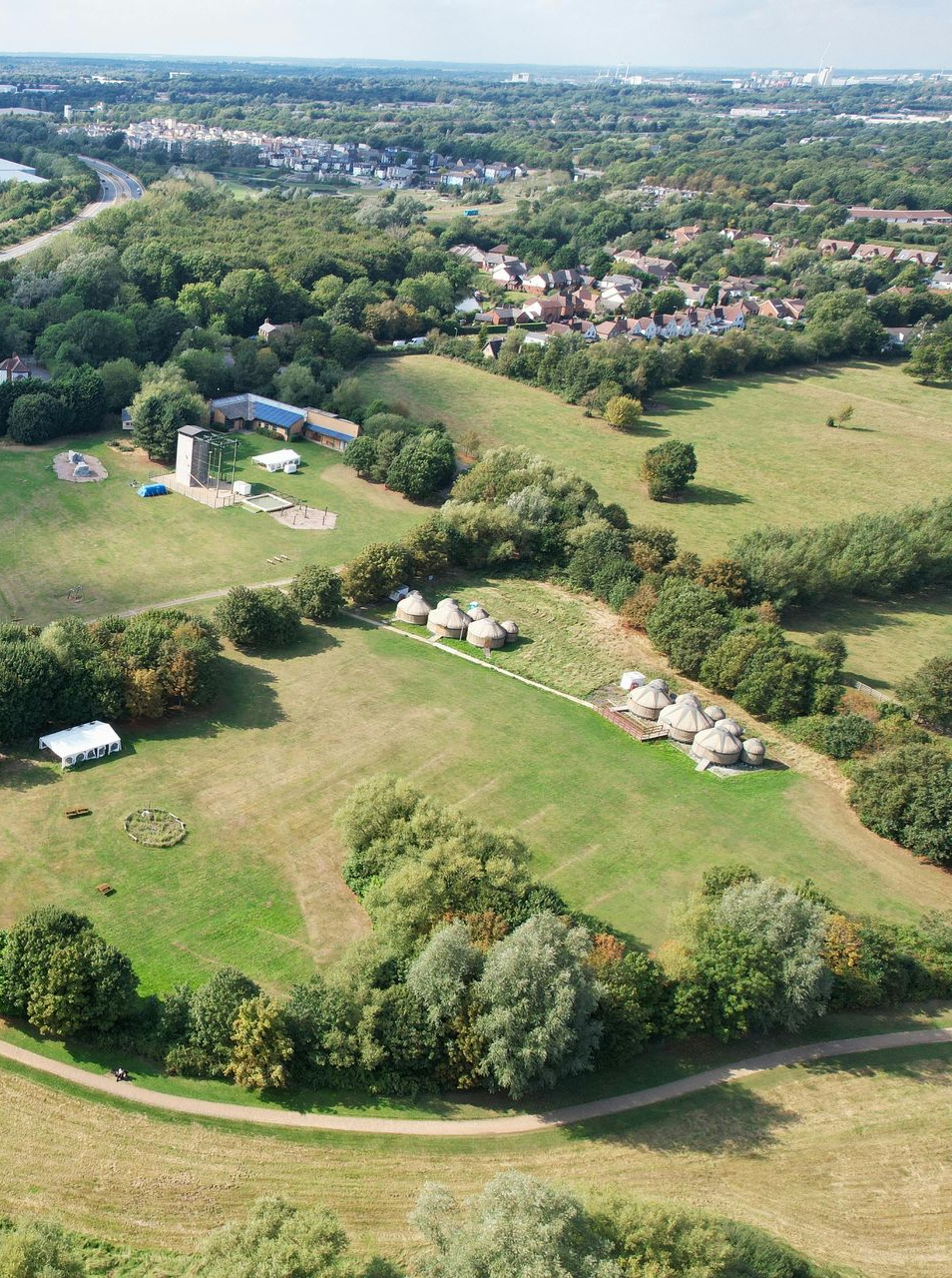 Aerial view of green fields, trees, and buildings, possibly a park or recreational area.