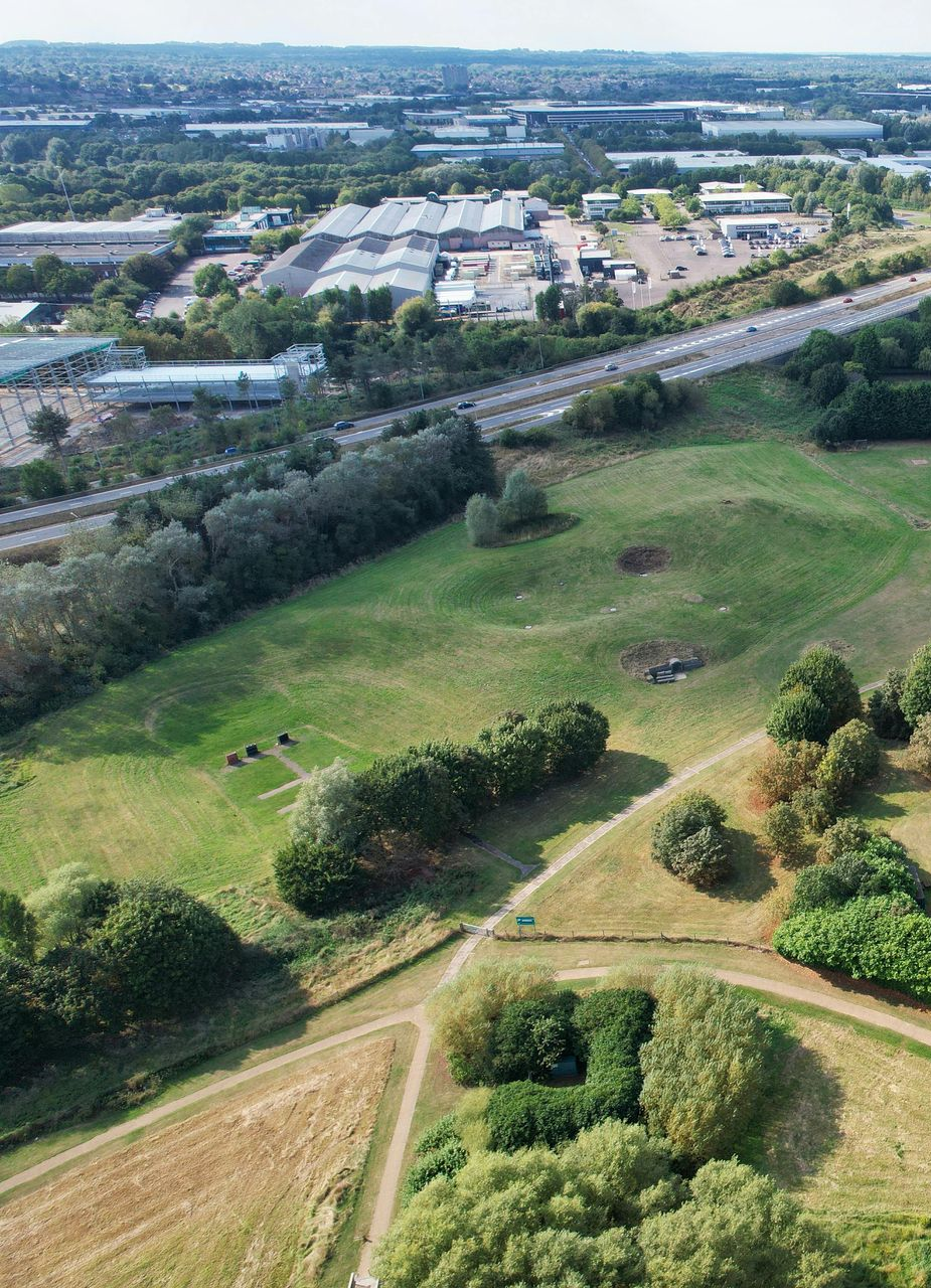 Green field with trees, a highway, and distant buildings on a sunny day.