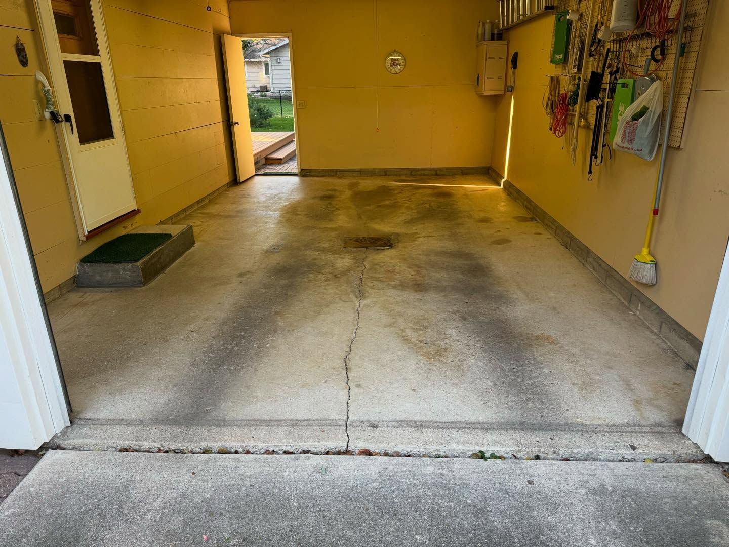 A garage interior featuring a light-colored concrete floor with dark tire tracks, a center crack, and an open doorway.