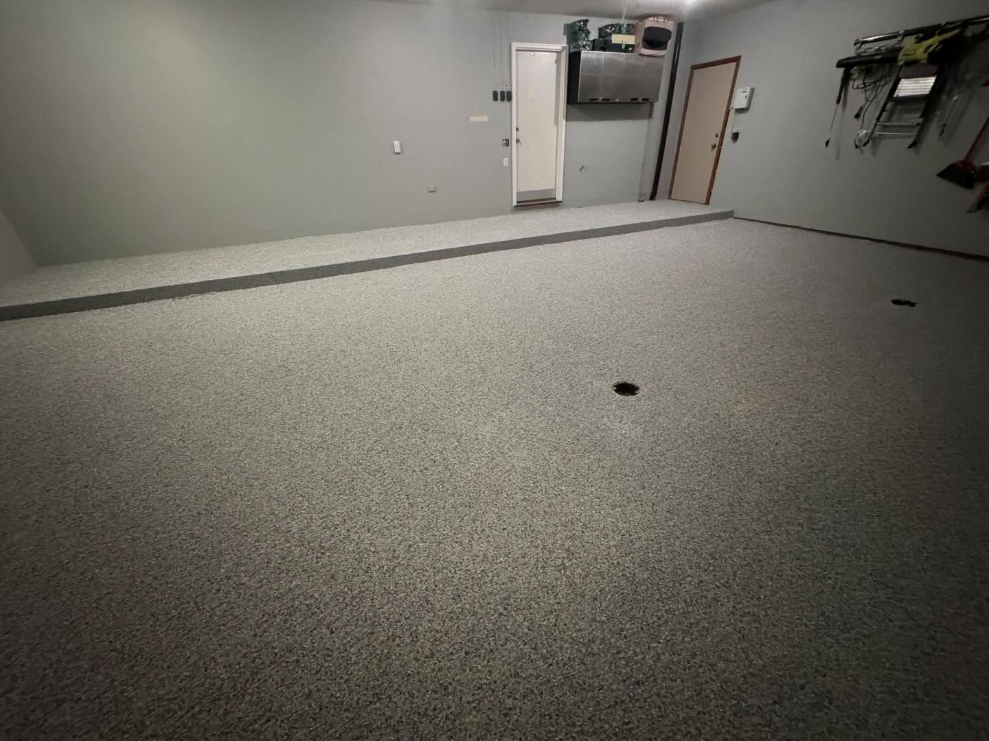A spacious garage interior featuring a freshly applied, speckled gray epoxy floor and light gray walls.