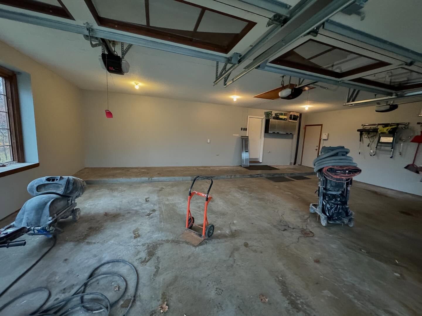 An empty garage undergoing floor renovations with concrete grinding equipment and tools present.