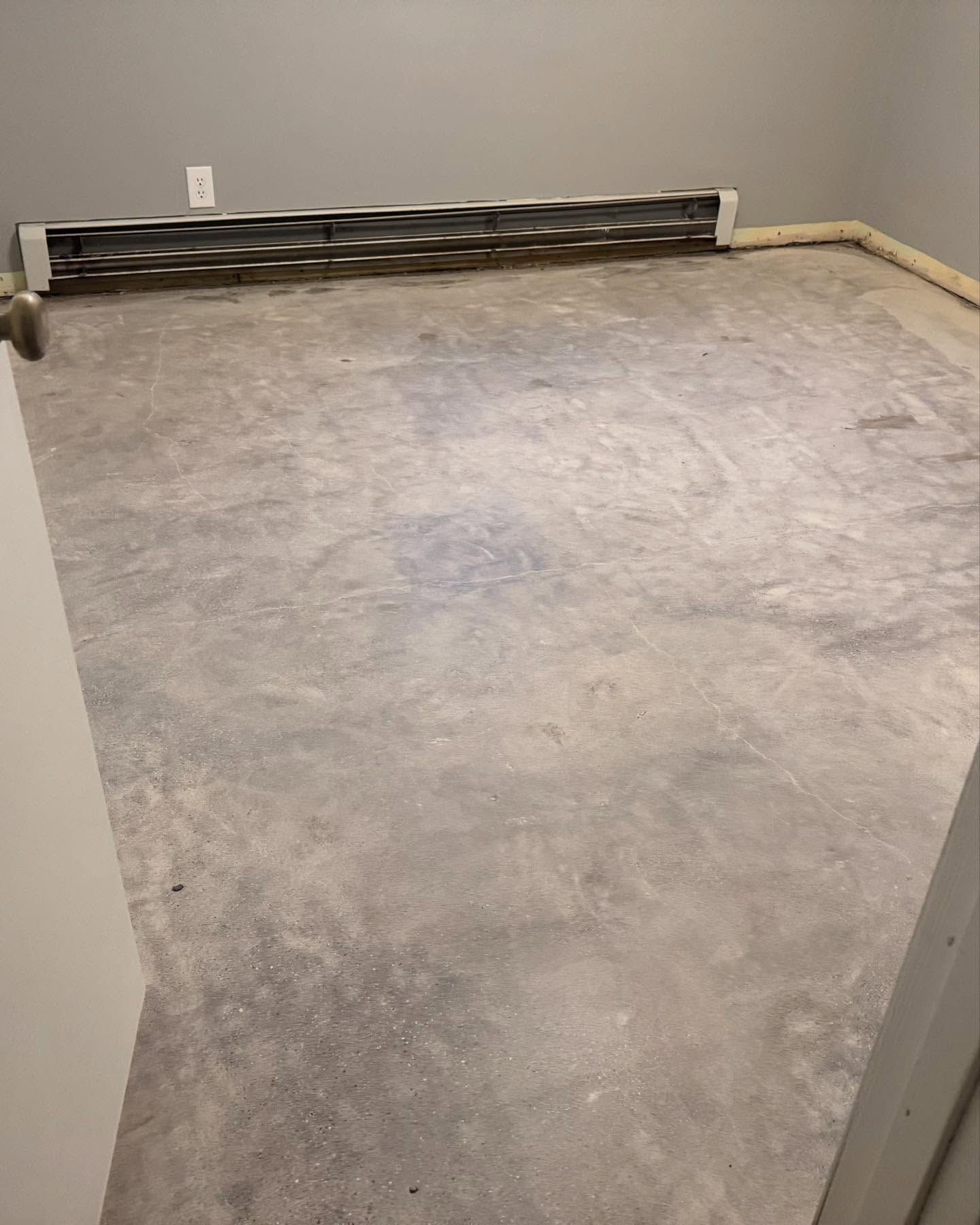 An empty room with gray concrete flooring and a baseboard heater installed along the far wall.