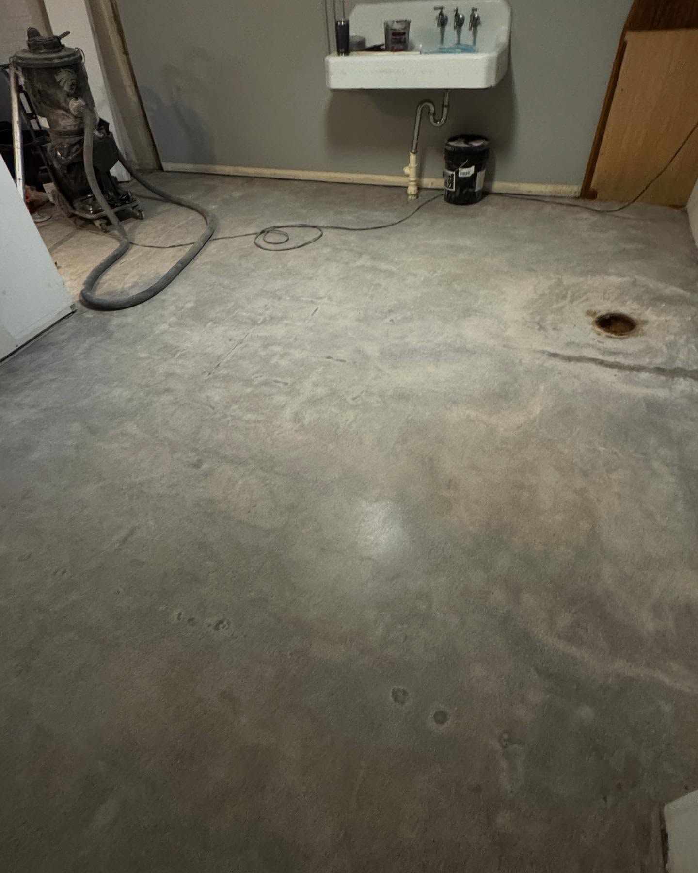 A workshop floor with a large utility sink on the back wall, a central drain, and a vacuum cleaner in the corner.