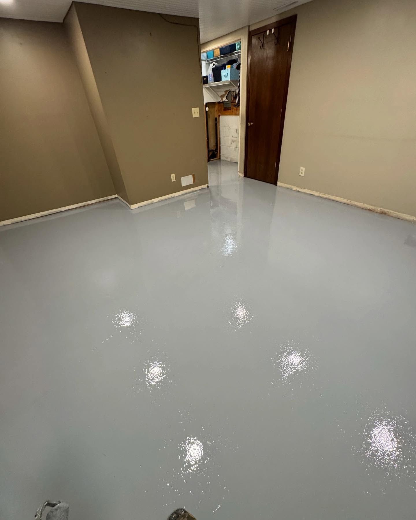 An interior room with a smooth, glossy, light gray epoxy floor reflecting the overhead lights, leading to a wooden door.