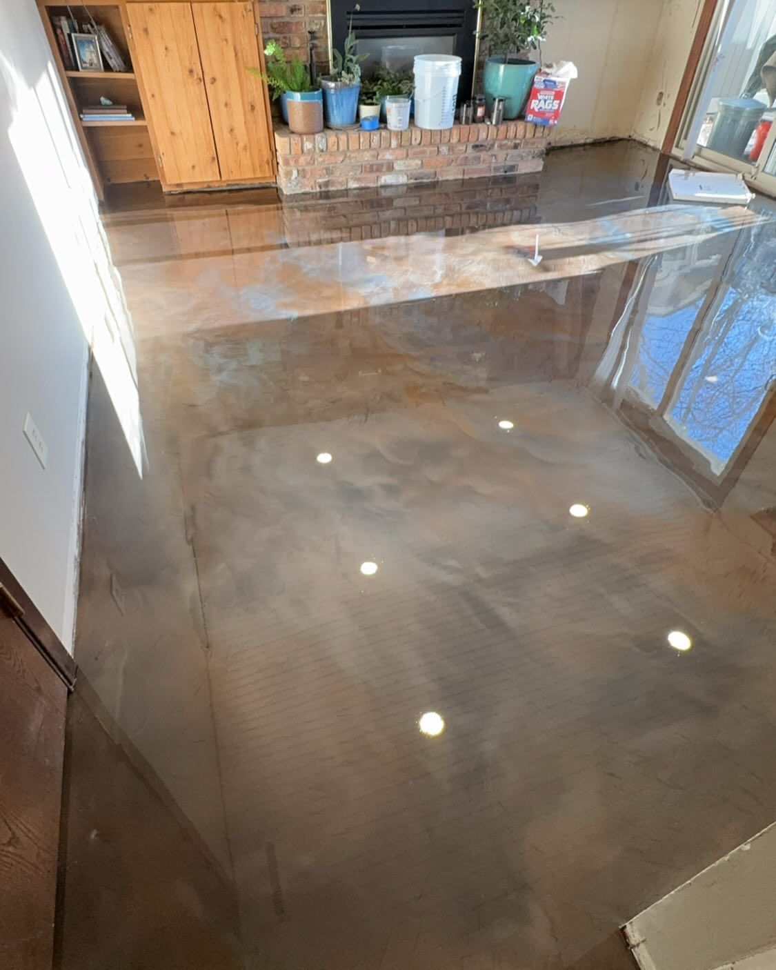 A high-gloss, metallic epoxy floor in neutral brown and gray tones reflects recessed lighting in a room with a fireplace.