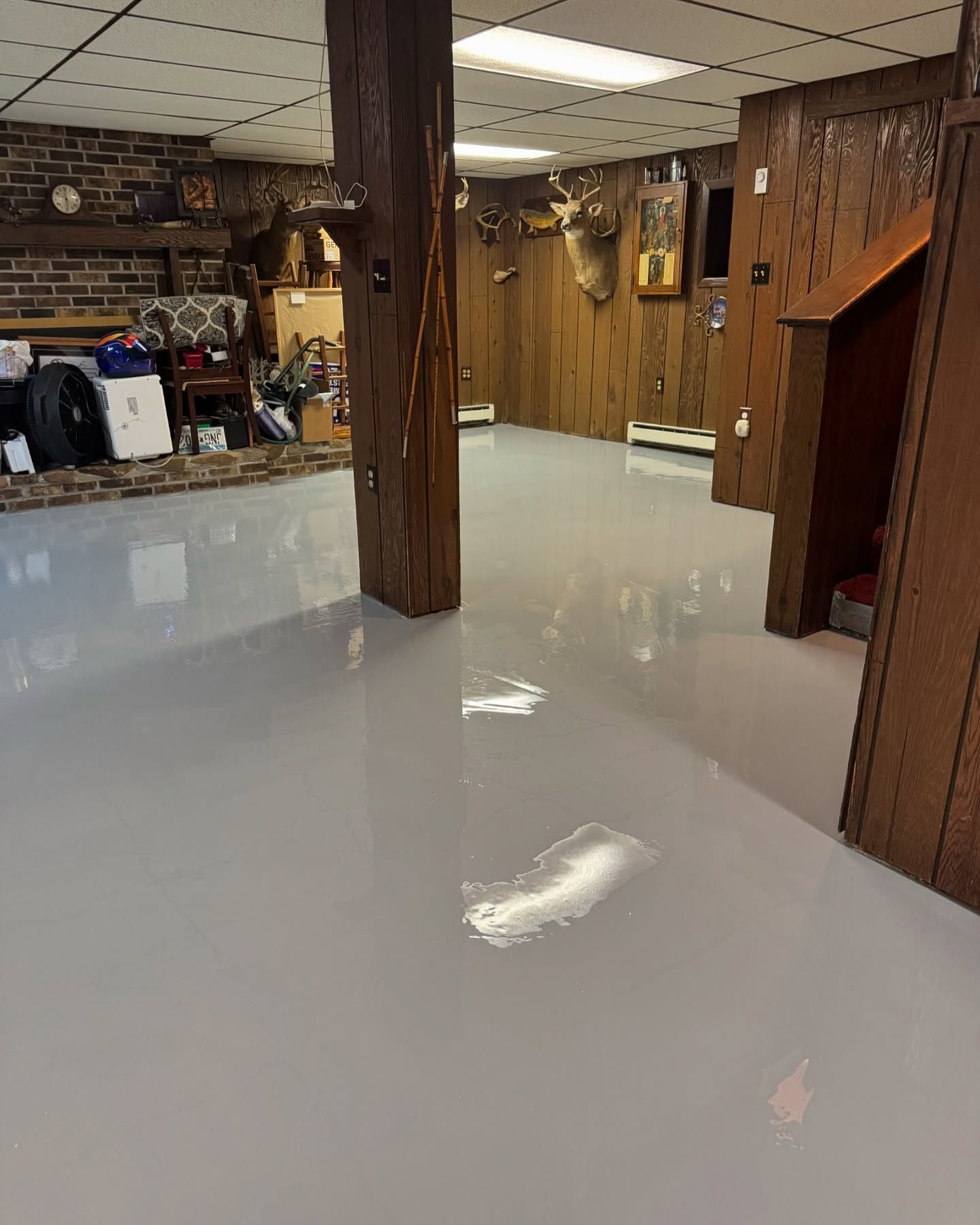A basement room with a glossy, light gray epoxy floor, wood-paneled walls, a brick fireplace, and a wooden support post.