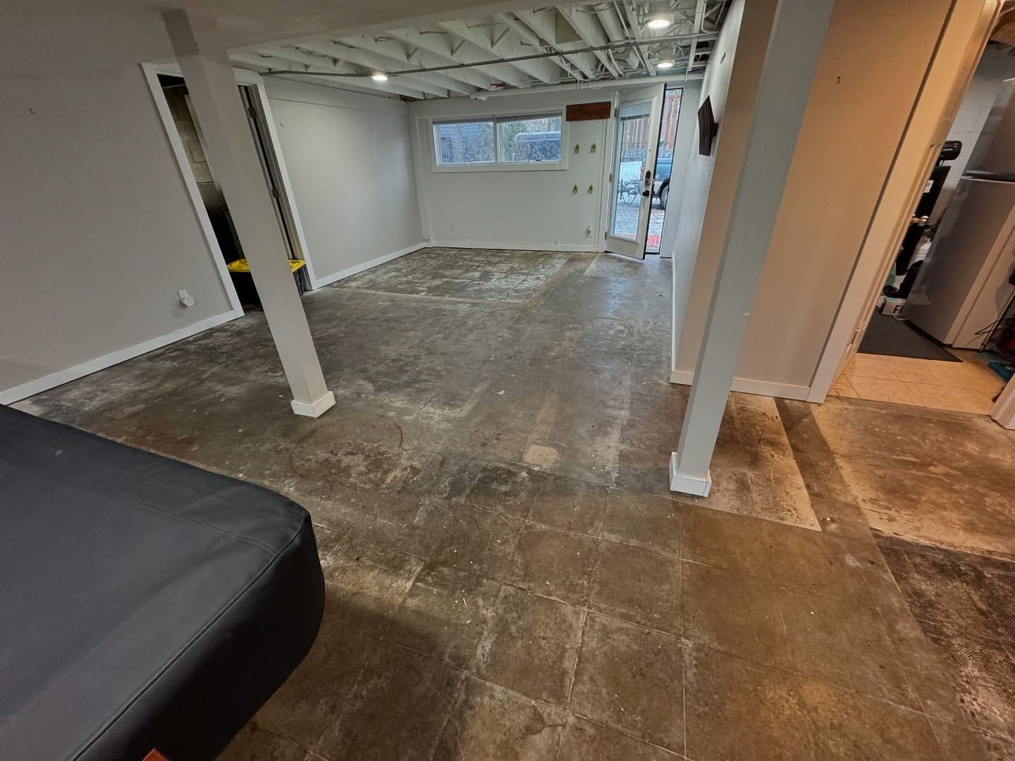 A spacious basement room with unfinished concrete flooring, gray walls, white support columns, and recessed lighting.