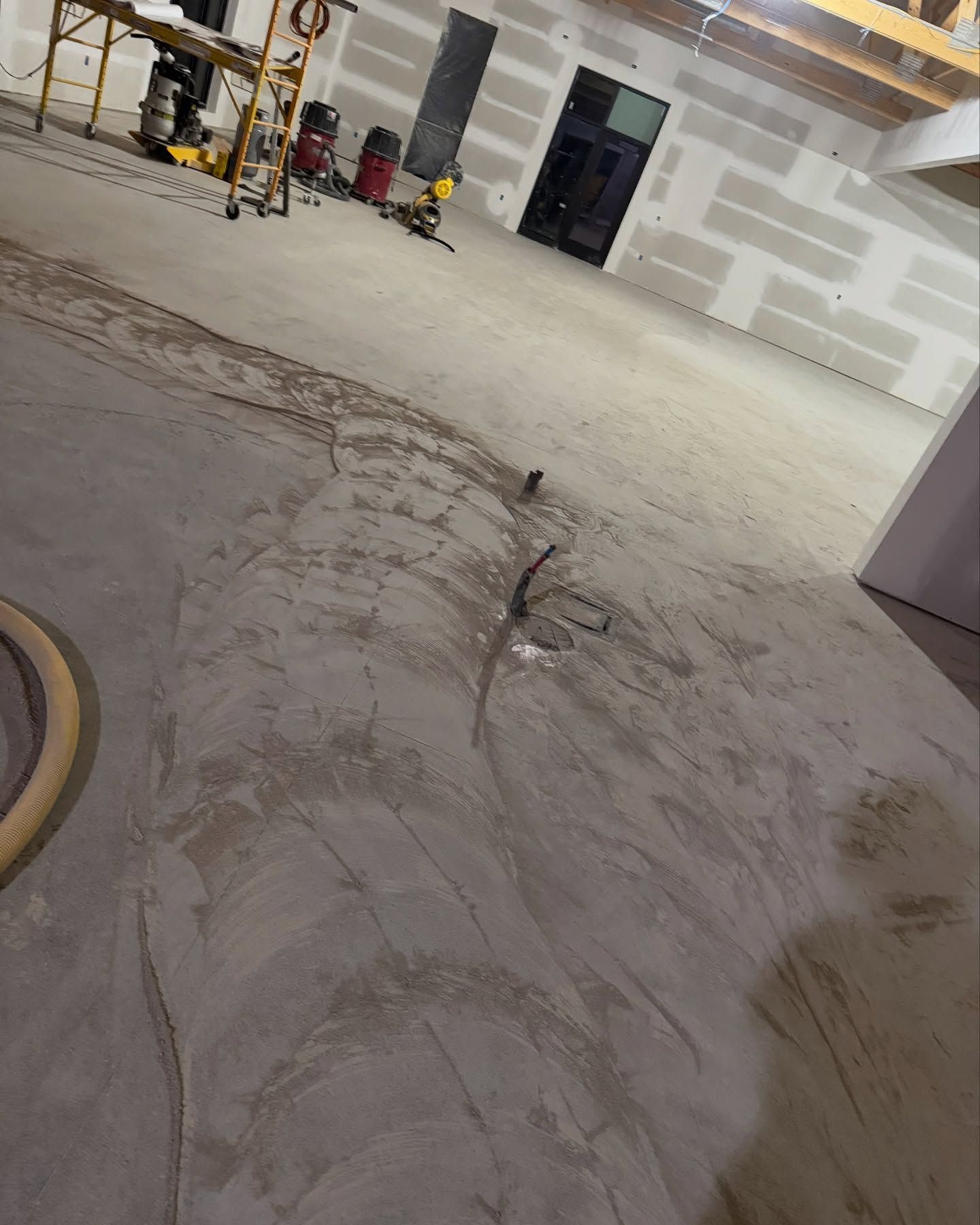 Construction site with unfinished concrete flooring, exposed wiring, and construction equipment in the background.