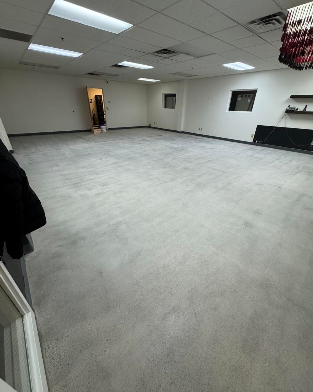 A spacious, empty room with light gray carpet, white walls, recessed ceiling lights, and a doorway at the far end.
